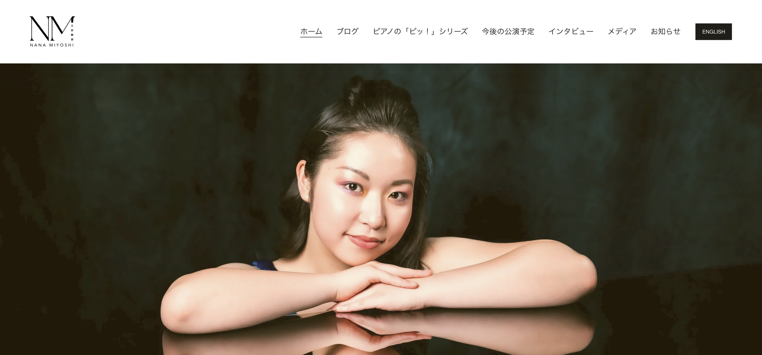 Portrait of a young woman with black hair, smiling softly, resting her arms on a reflective surface against a dark background.
