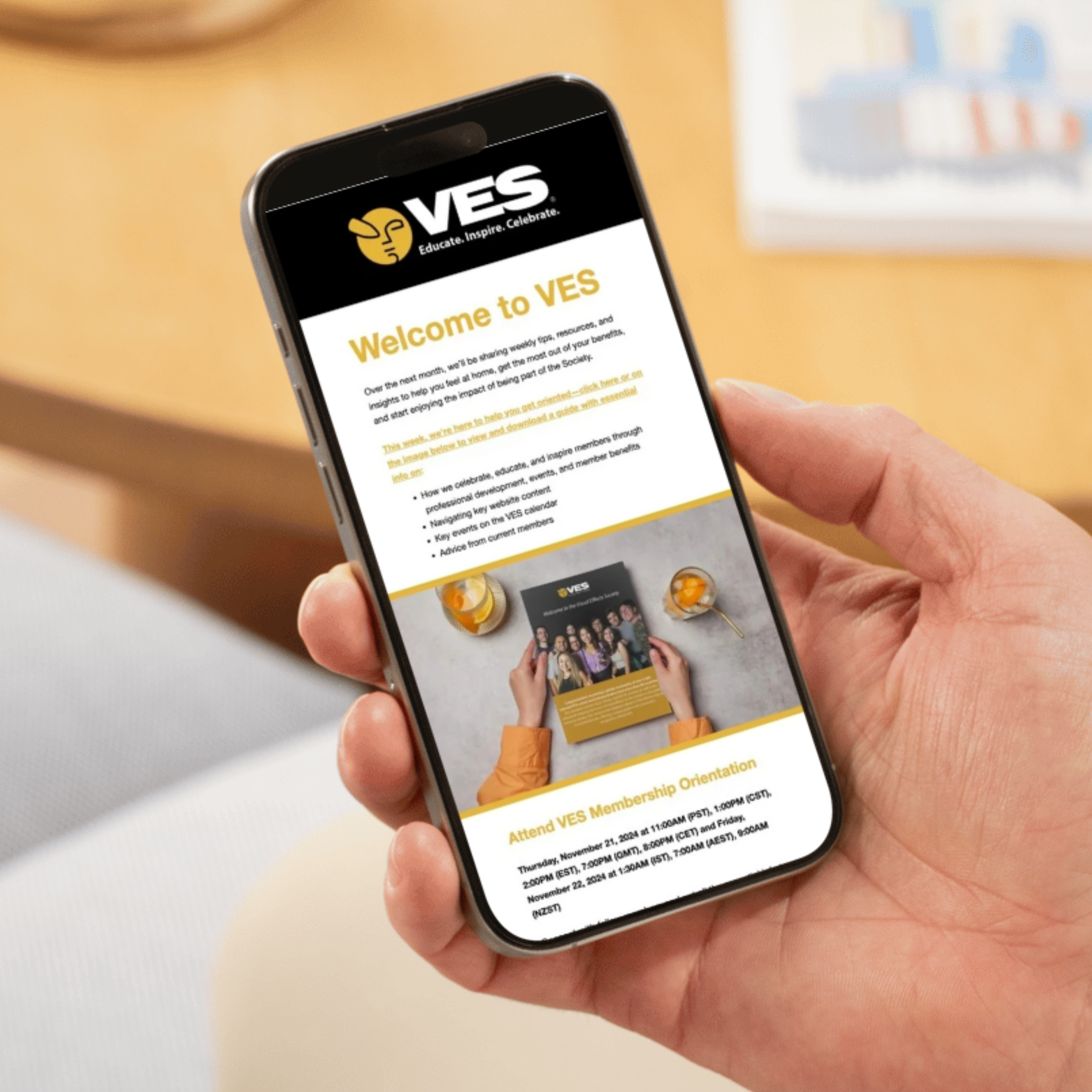 Close-up of a person's hand holding a smartphone displaying a website for VES with an orange and black color theme, showing community event information on a beige background.