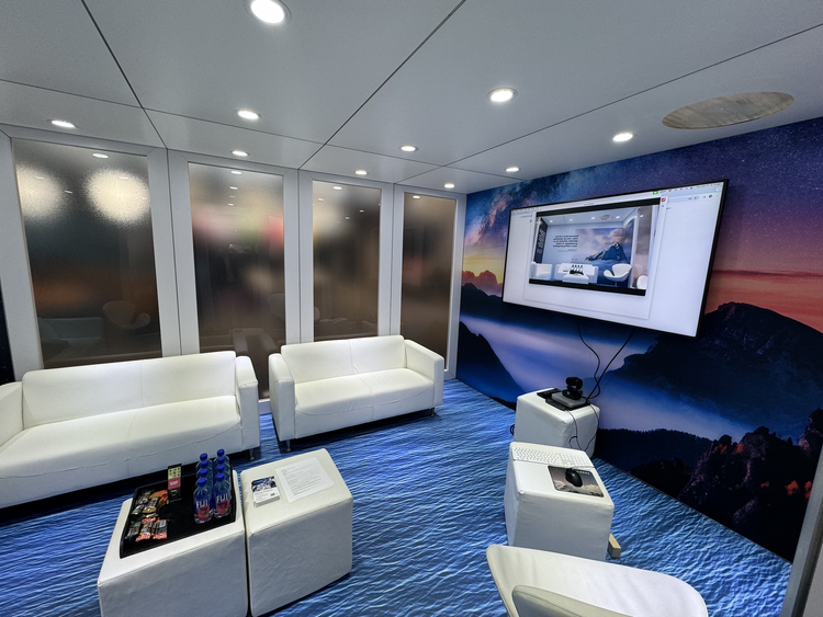 Modern meeting room with white sofas, a large wall screen, and a mountain landscape mural