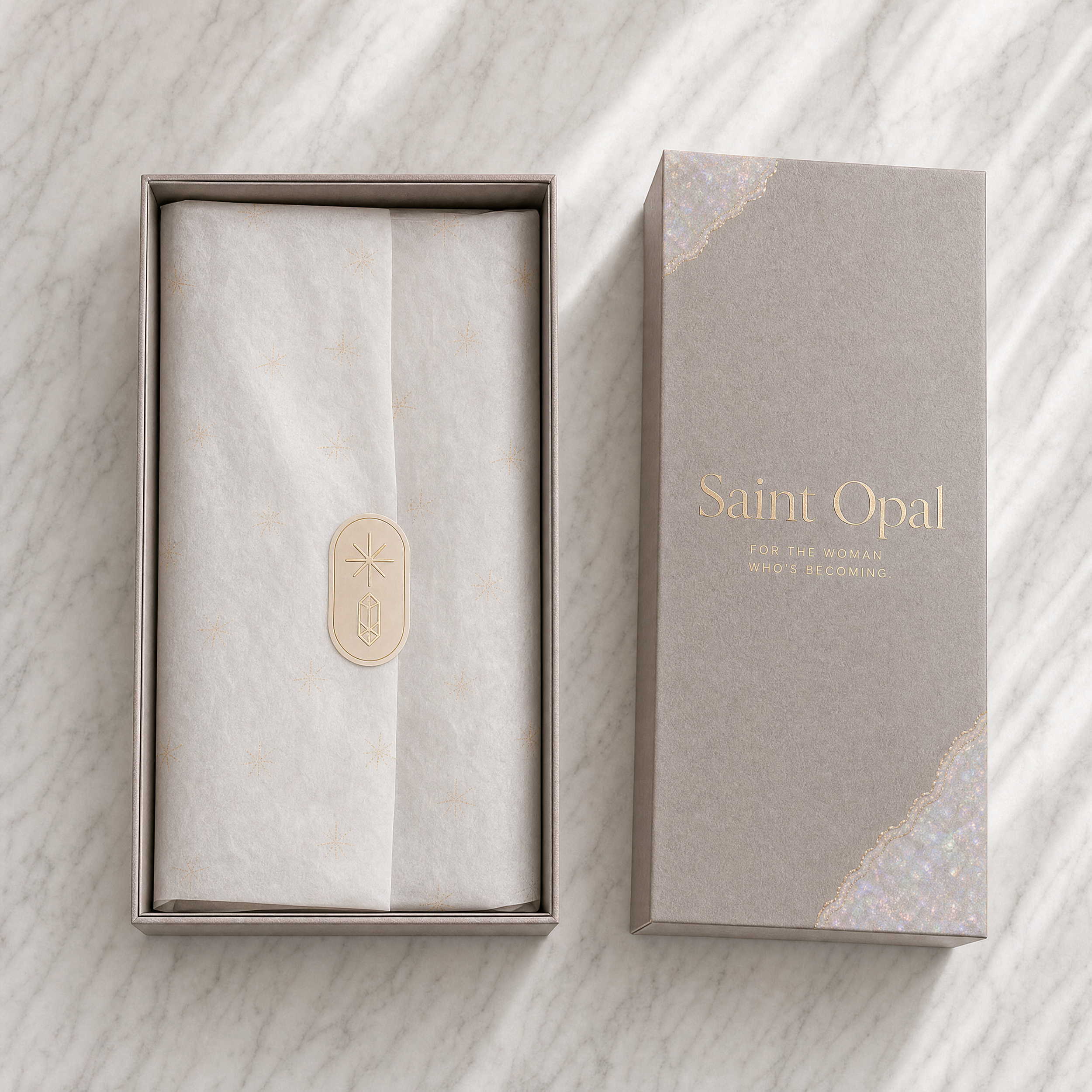 Open jewelry box with wrapped item inside on a marble surface, next to a closed box with "Saint Opal" written on it.
