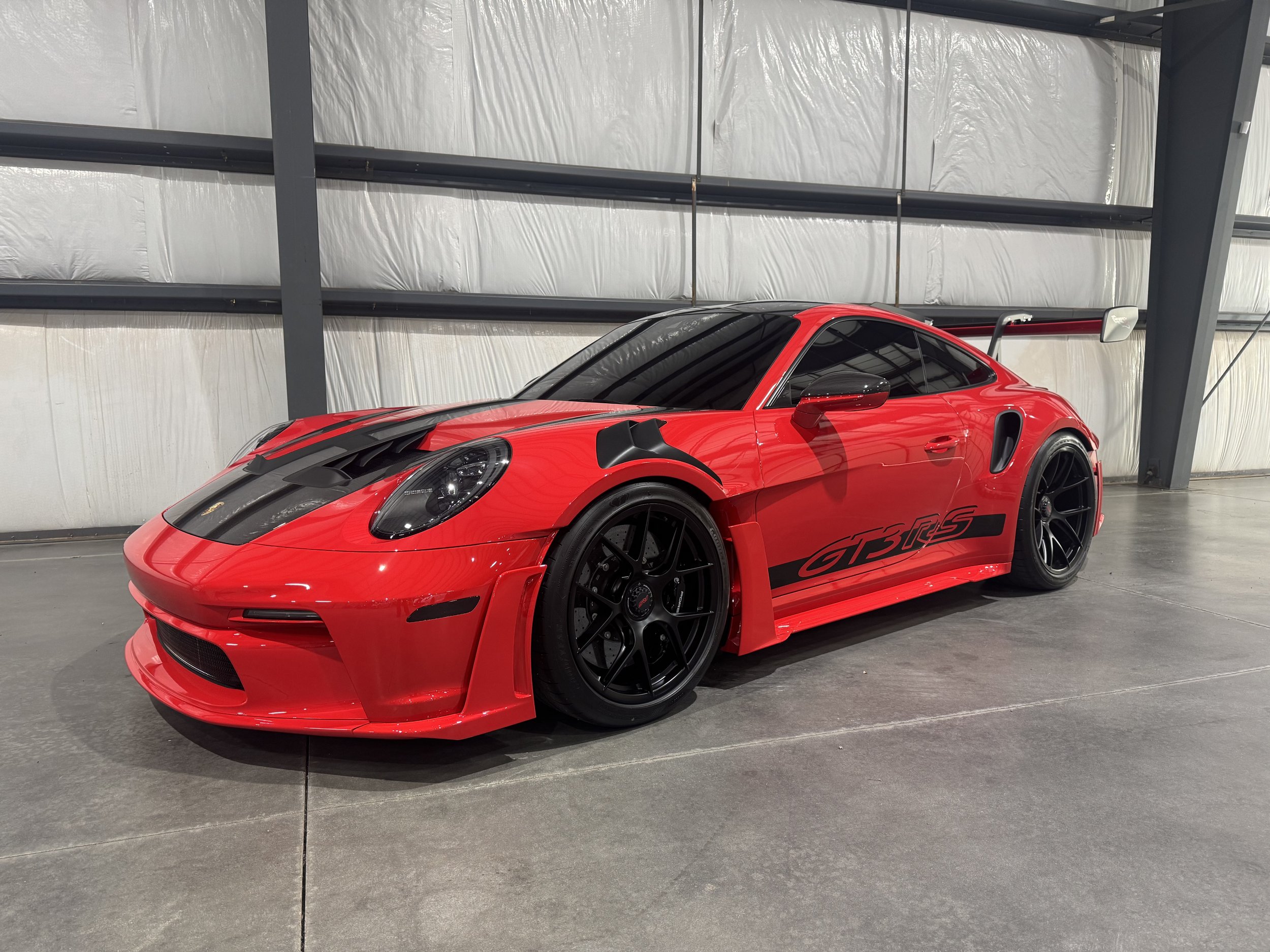 Red Porsche GT3 RS sports car inside a showroom with a gray metal structure and white insulation walls.