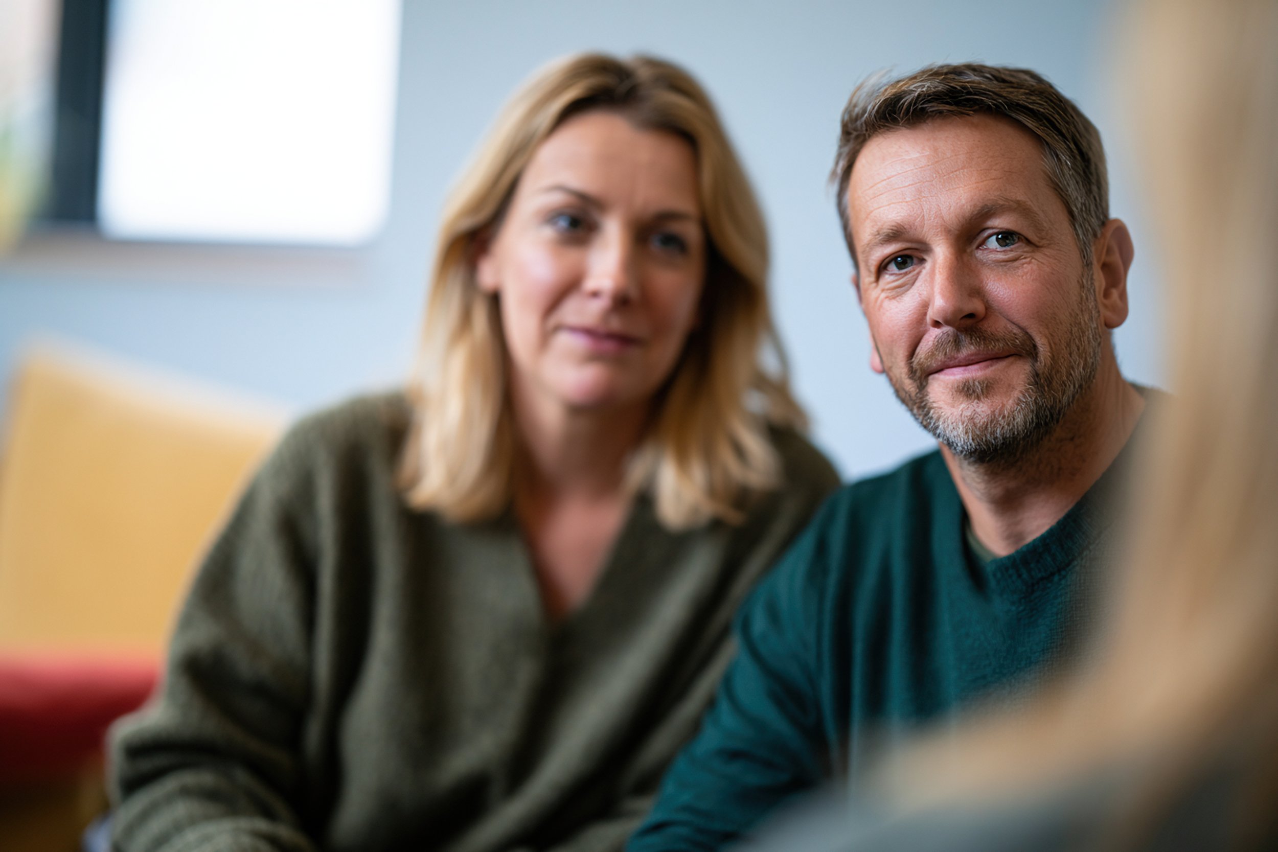Man and woman sit together and look at a blurry therapist in the foreground