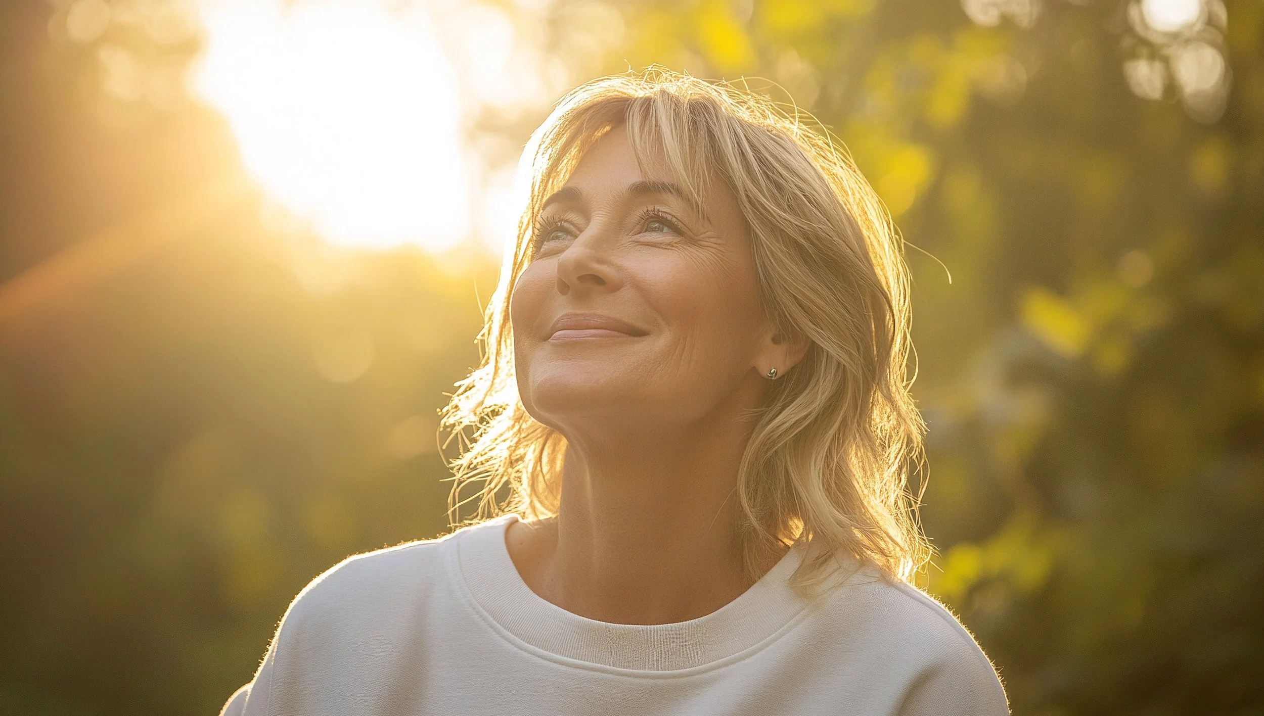 Middle-aged woman looks up and to the left with a hopeful smile, backlit by the sun