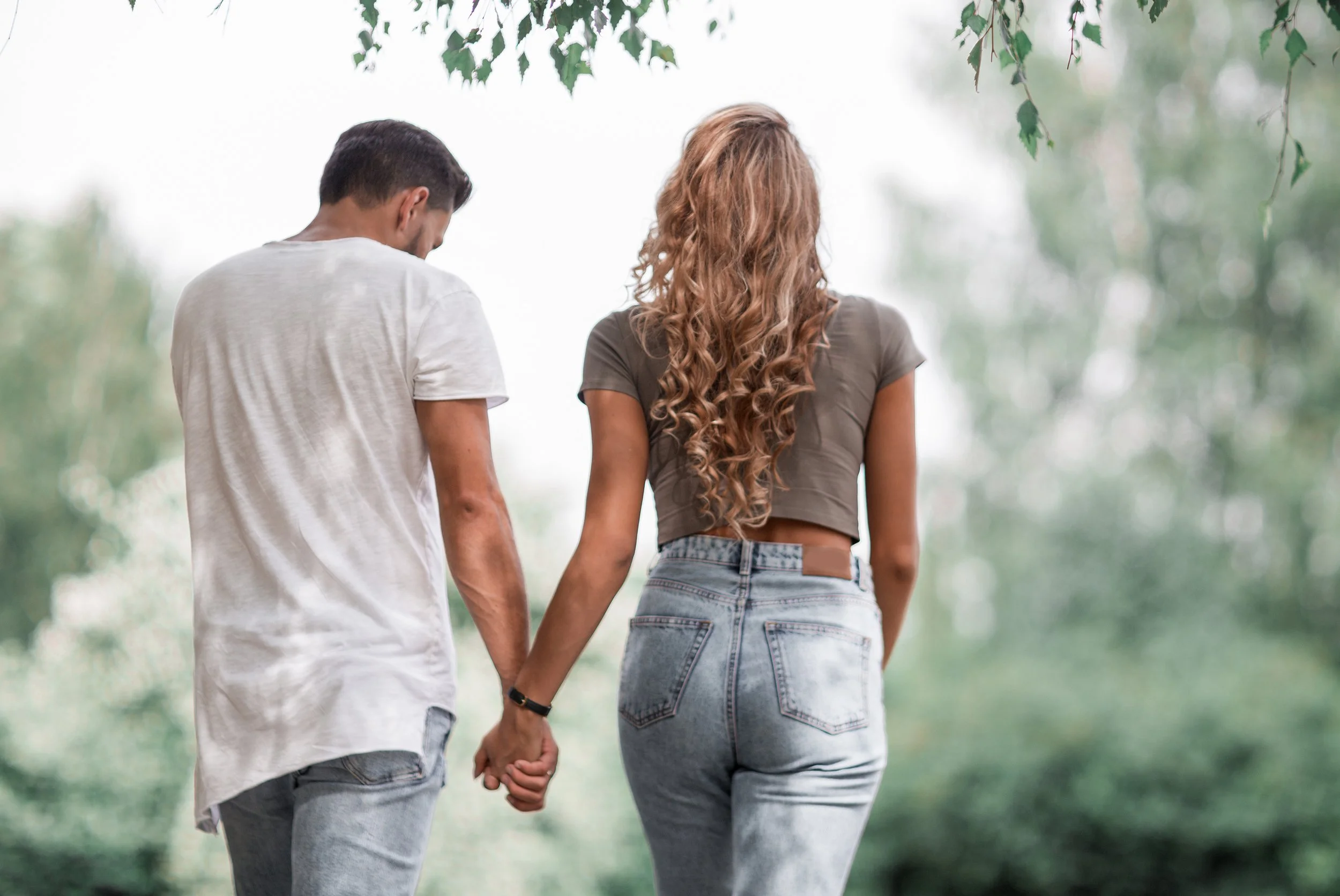 Man and woman holding hands walking away from the camera in a lush garden