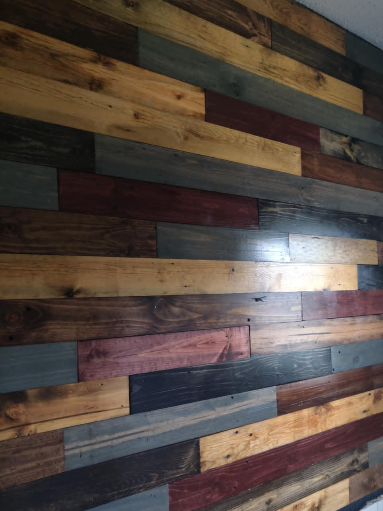 Colorful wooden plank flooring with a mix of natural wood and stained colors, arranged in a staggered pattern.