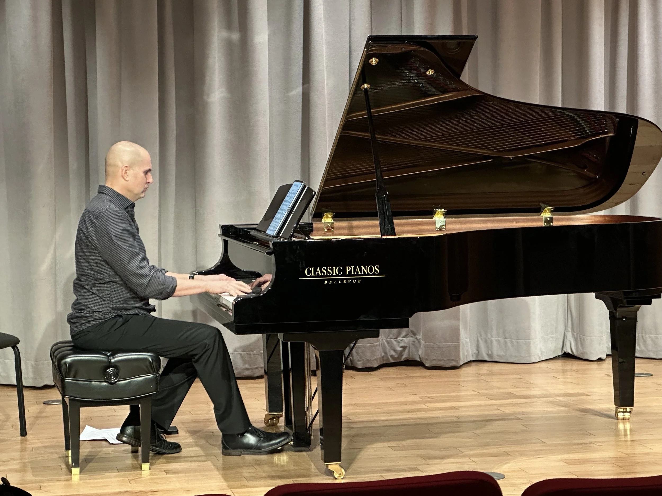 Ron Leonardi playing the piano on a stage with a grey curtain backdrop.