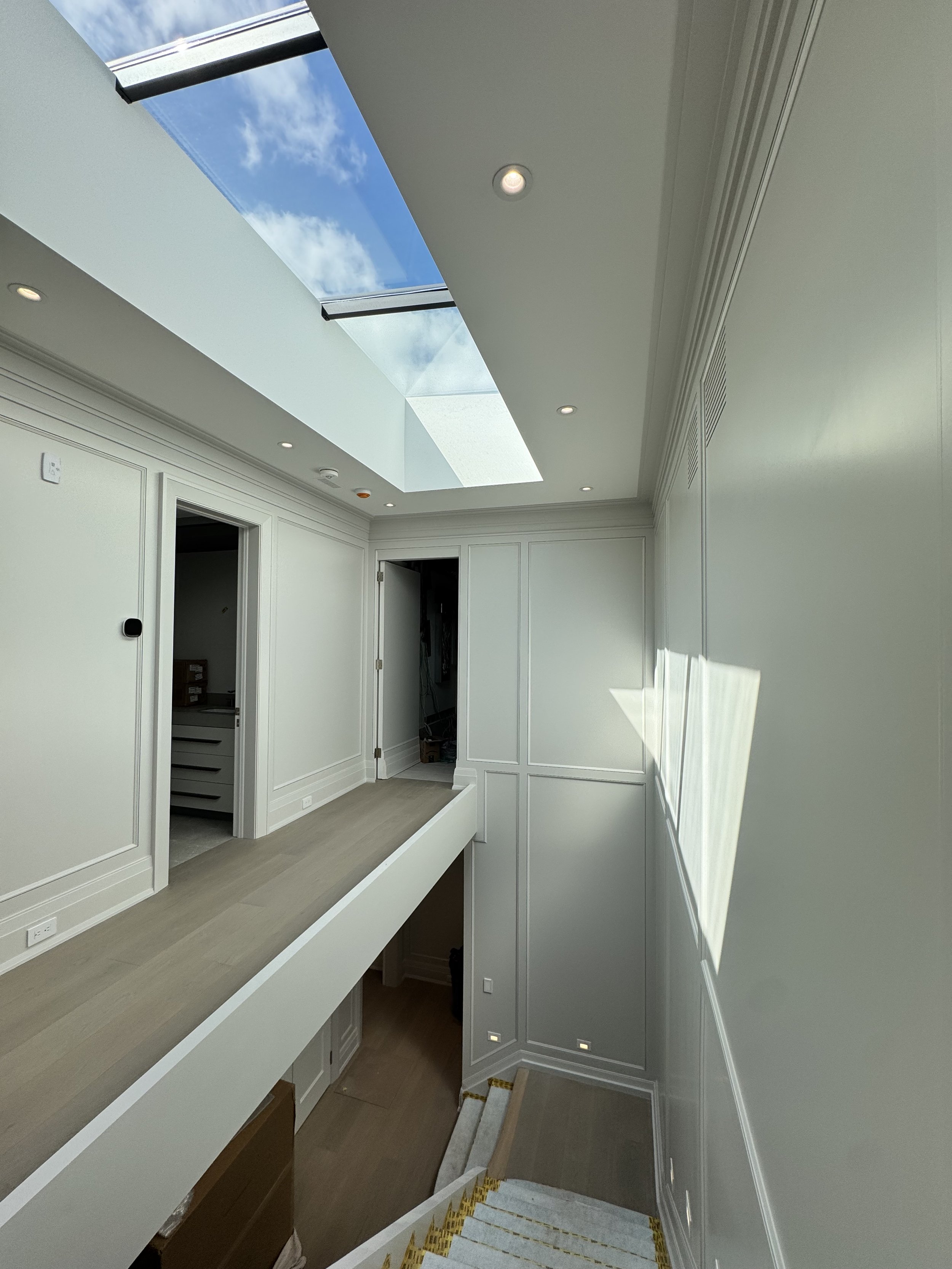 Interior view of a modern staircase with a skylight overhead, providing natural light to the white-walled hallway.