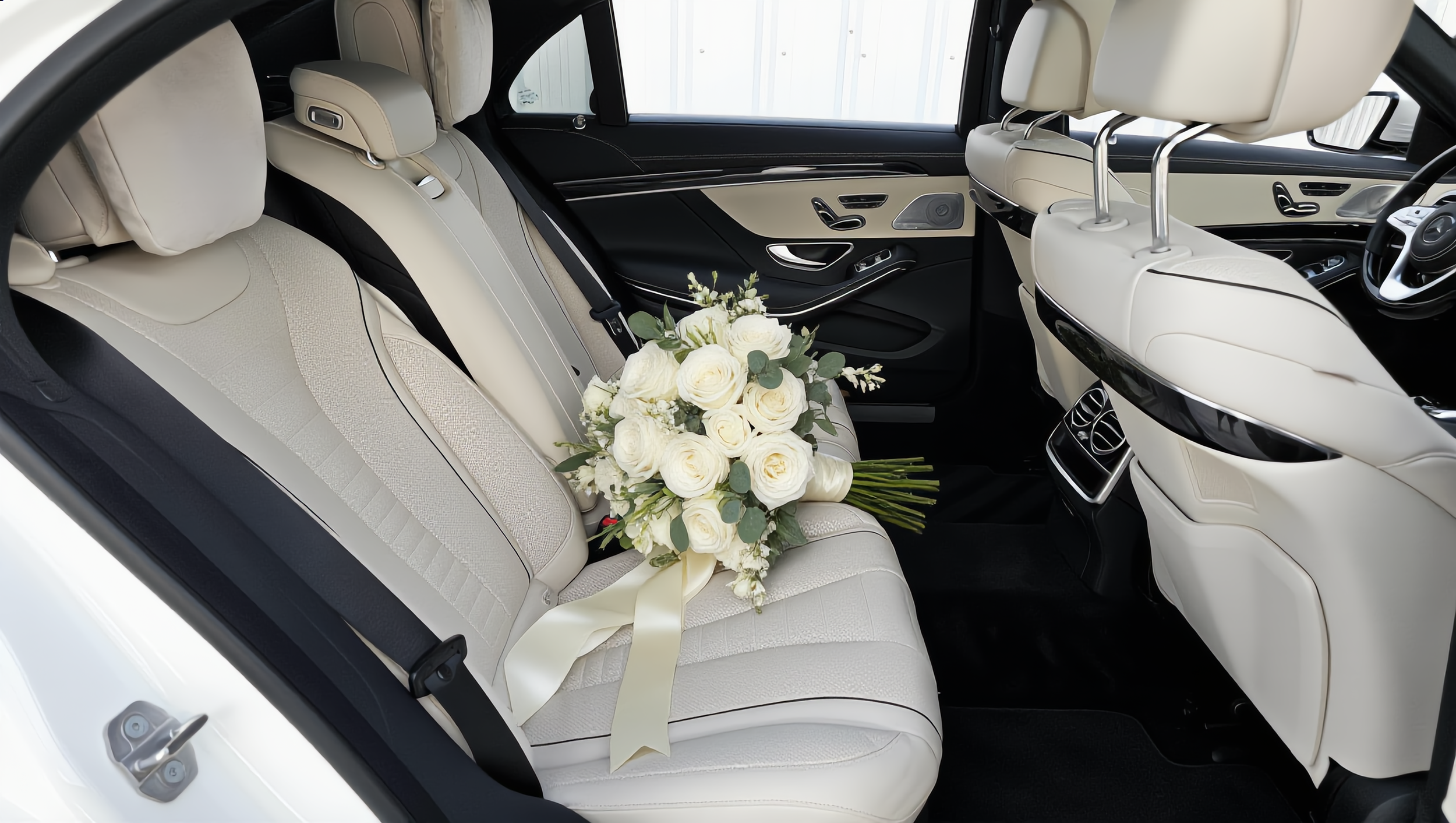 Interior of a luxury car Mercedes-Benz S560 with cream-colored leather seats, black accents, and a bouquet of white roses on the rear seat.