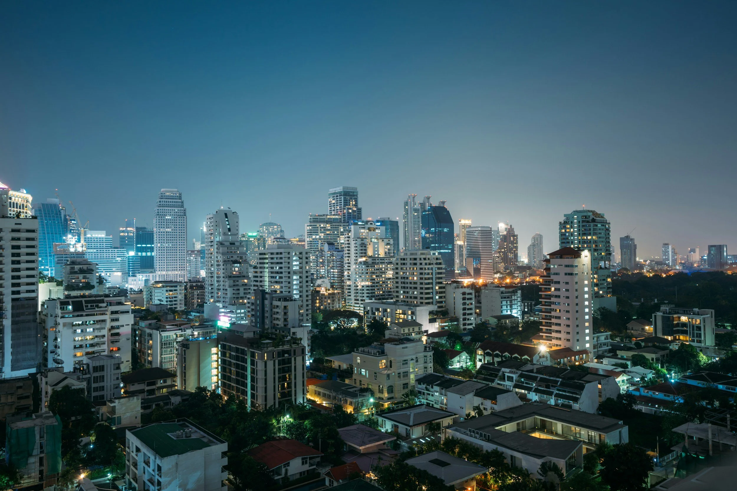Night view of a city skyline with illuminated high-rise buildings and residential structures.
