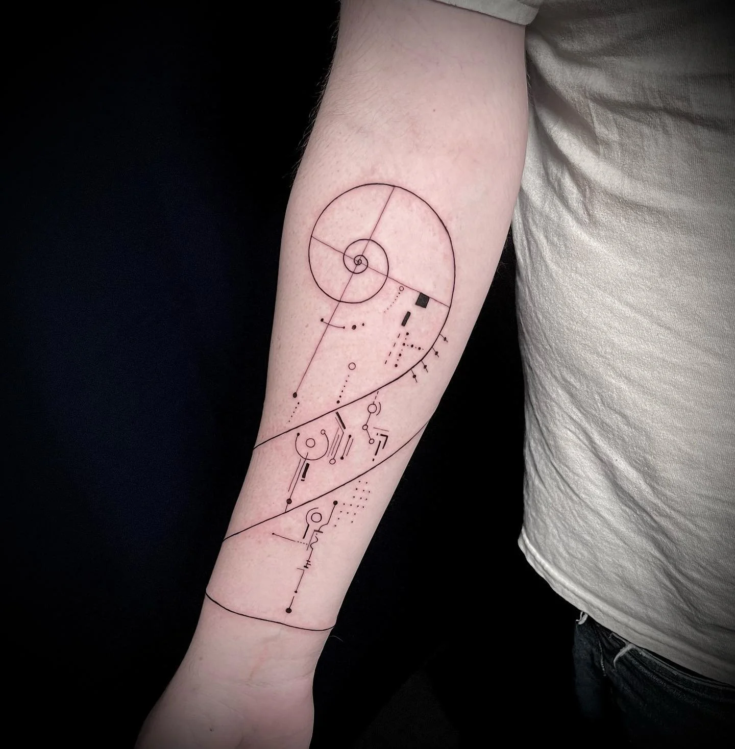 A tattoo of a geometric and abstract design with circles, lines, and dots on a person's forearm.