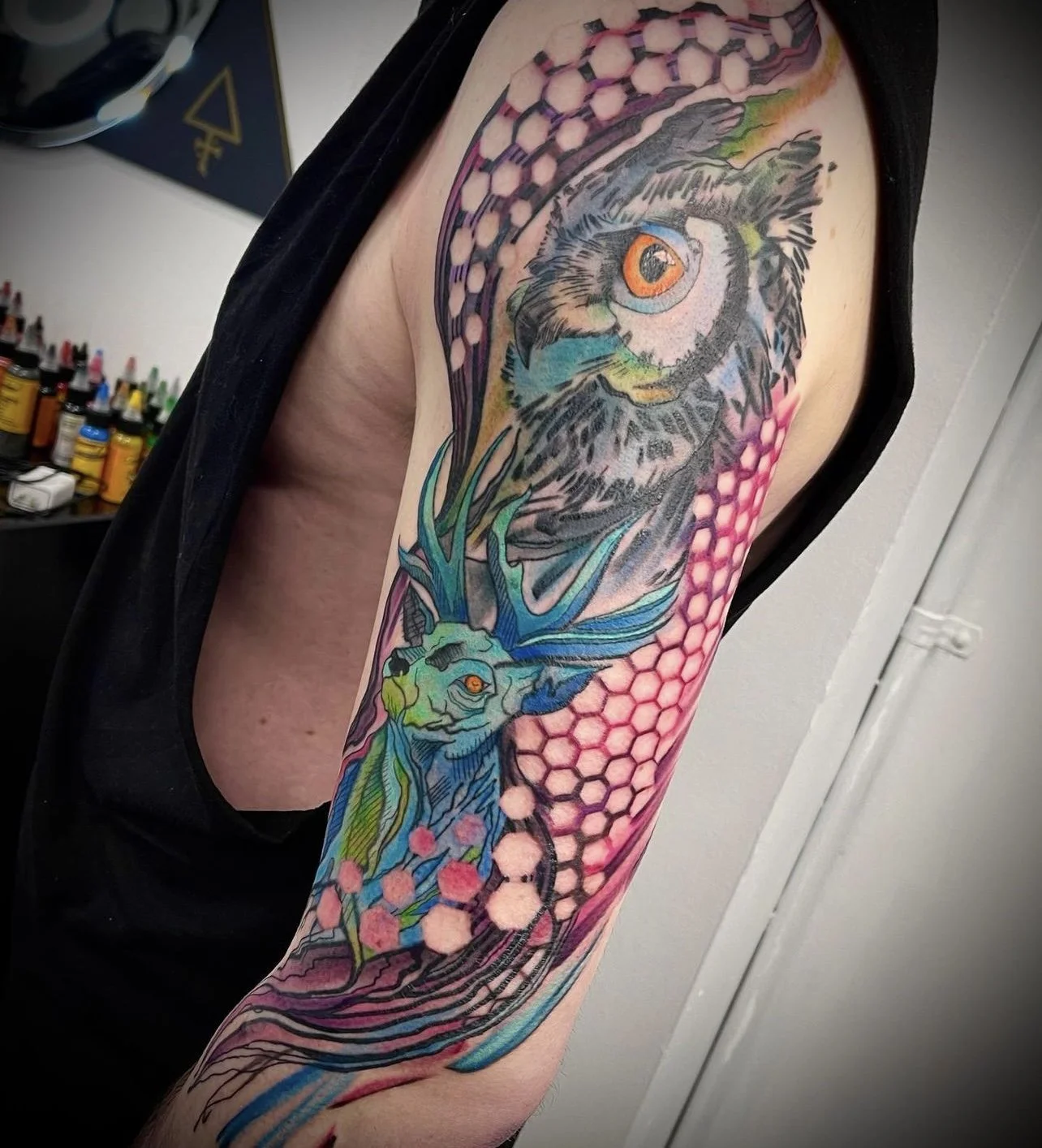 Colorful tattoo of an owl and a deer with geometric patterns on upper arm.