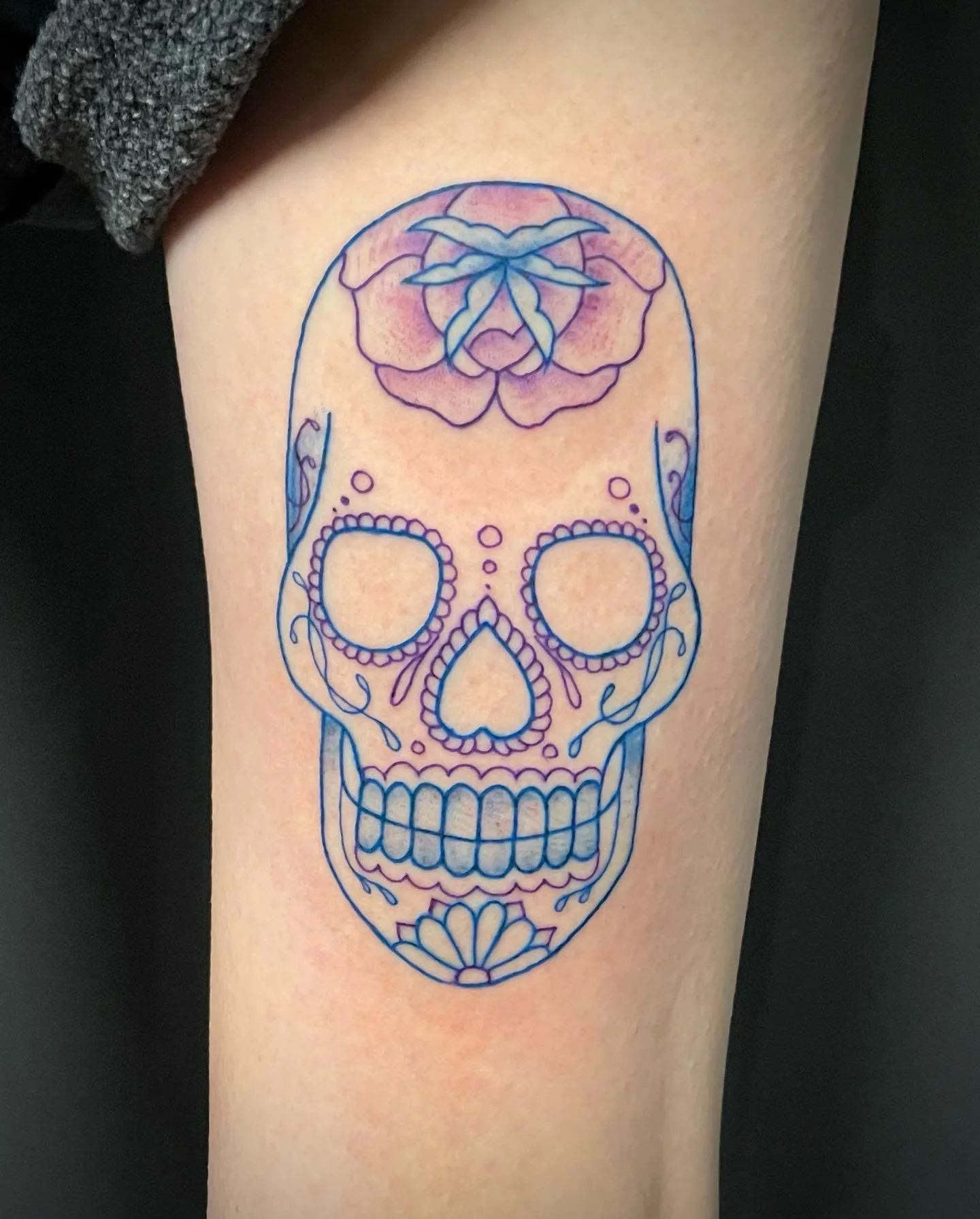 Tattoo of a decorative skull with floral elements on person's arm.