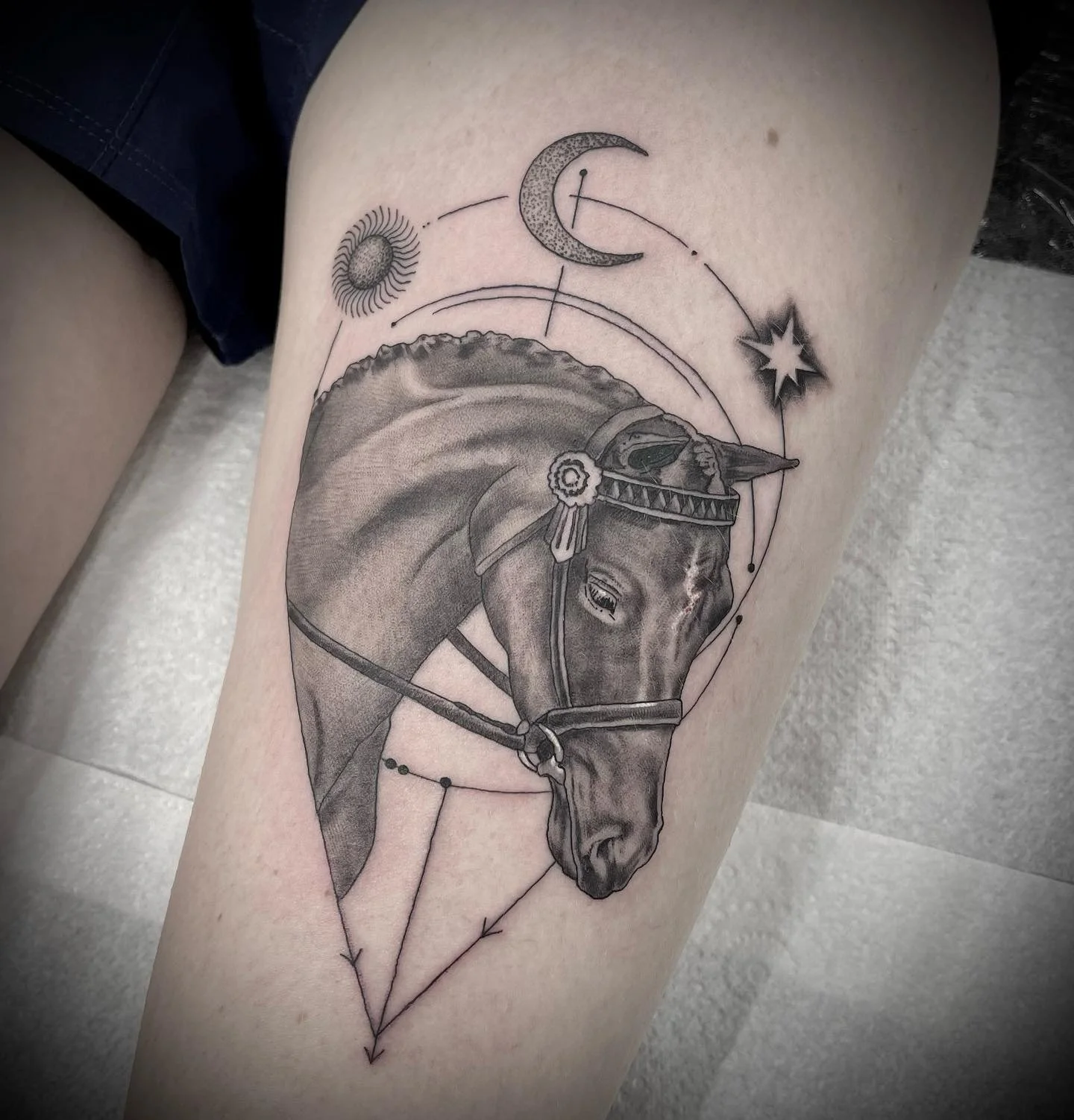 Black and gray tattoo of a horse's head with celestial elements including the sun, moon, star, and planets, with geometric lines and shapes around the horse.