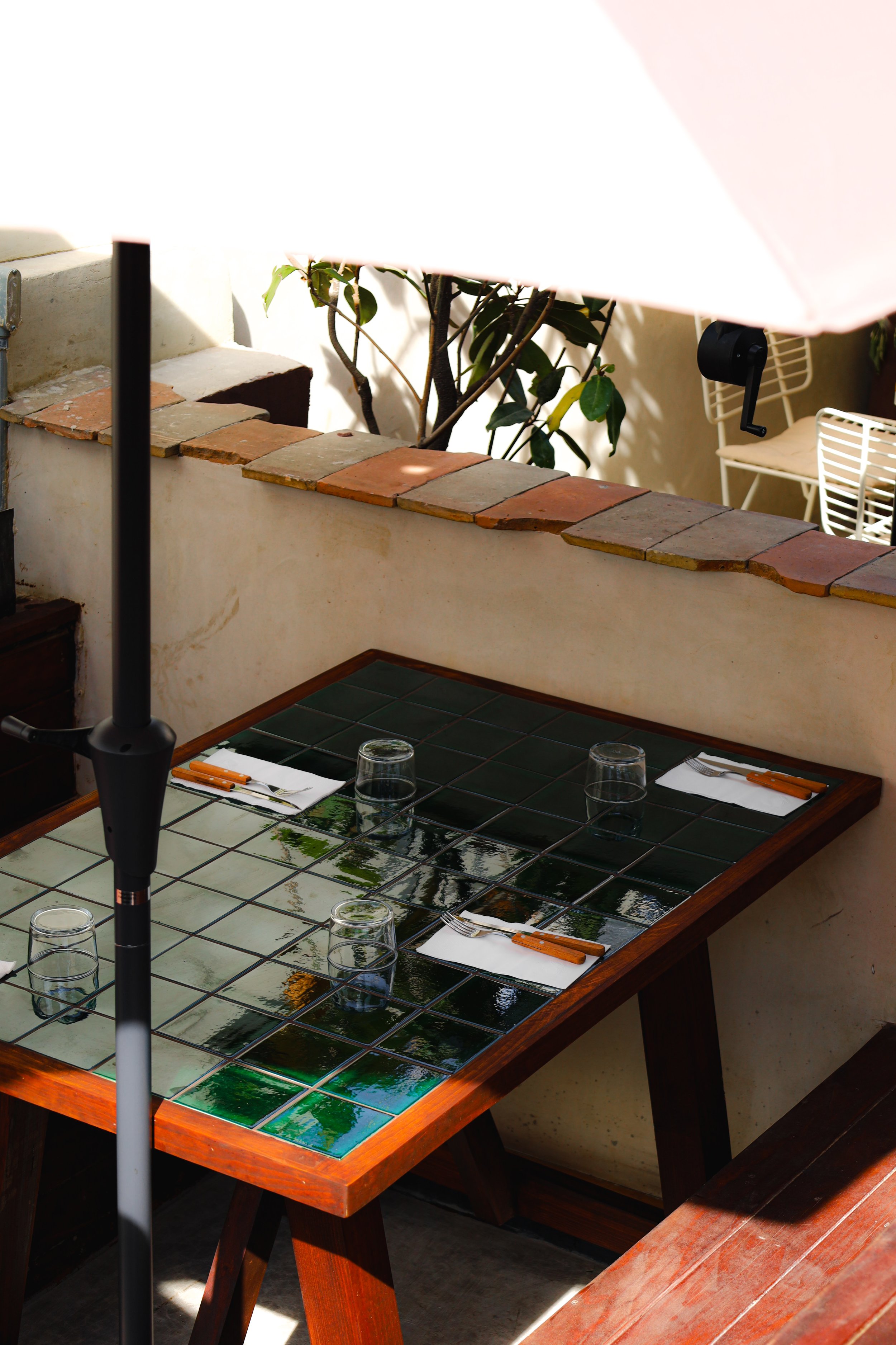 Mesa de comedor con platos, cubiertos y vasos en un restaurante con decoración moderna y plantas en la esquina.