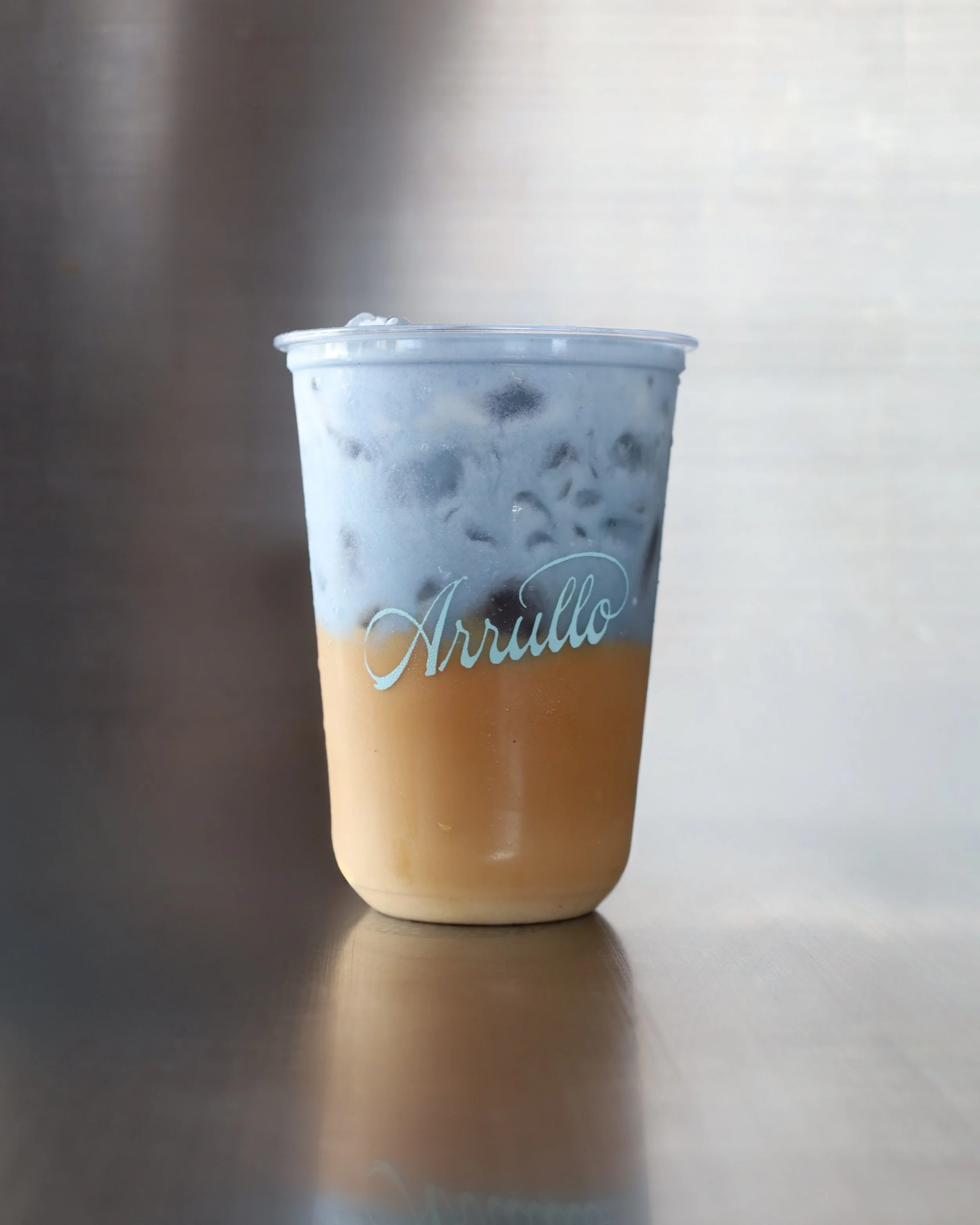 Vaso de bebida fría de nuestro latte de la casa con un cold foam azul, con la palabra Arrullo escrita en letras blancas.