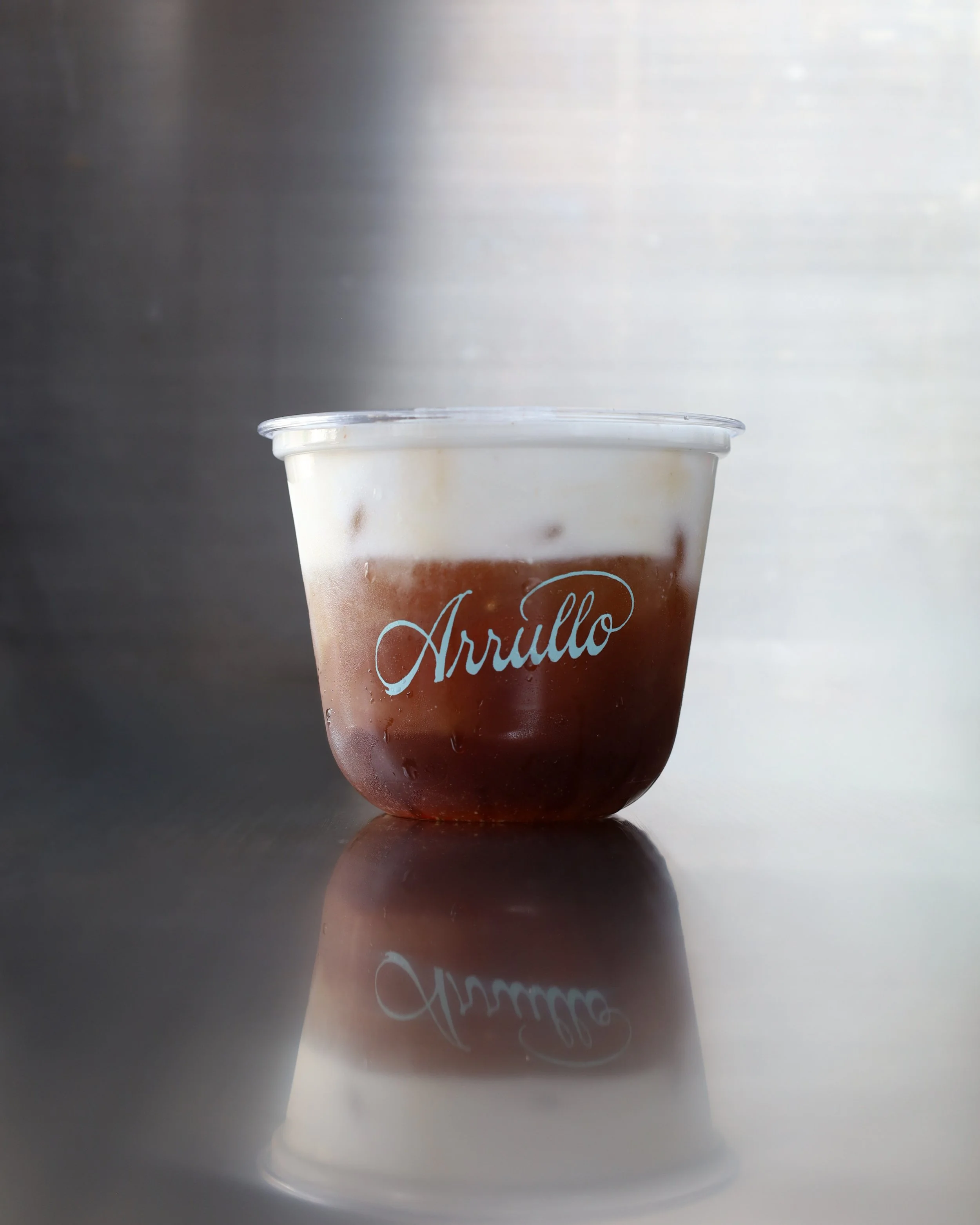Vaso de bebida fría lleno de café cold brew con un cold foam de vainilla y la palabra 'Arrullo' escrita en letra cursiva en la parte frontal.
