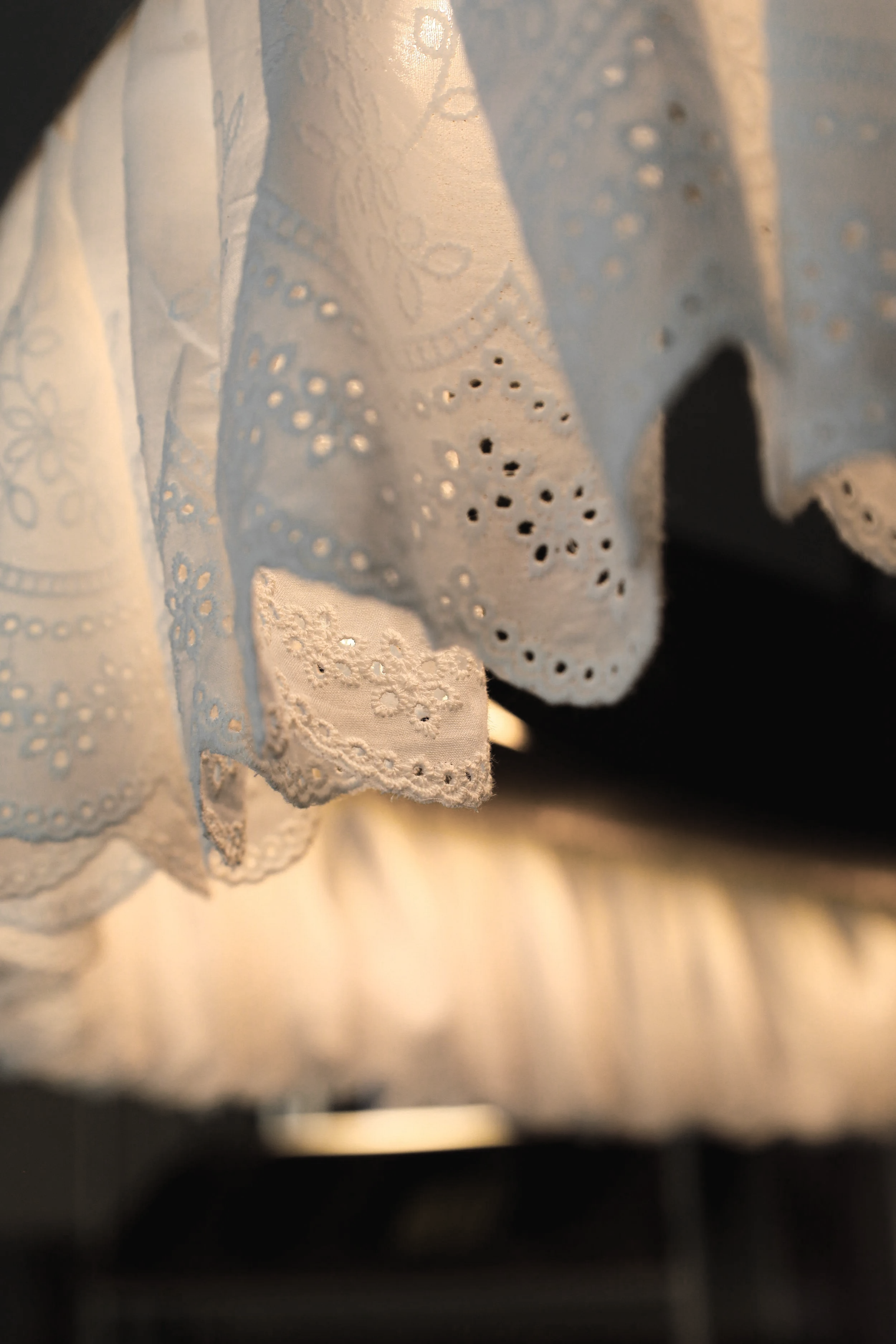 Tela de encaje blanco con bordados y detalles de perforaciones, en un fondo oscuro.