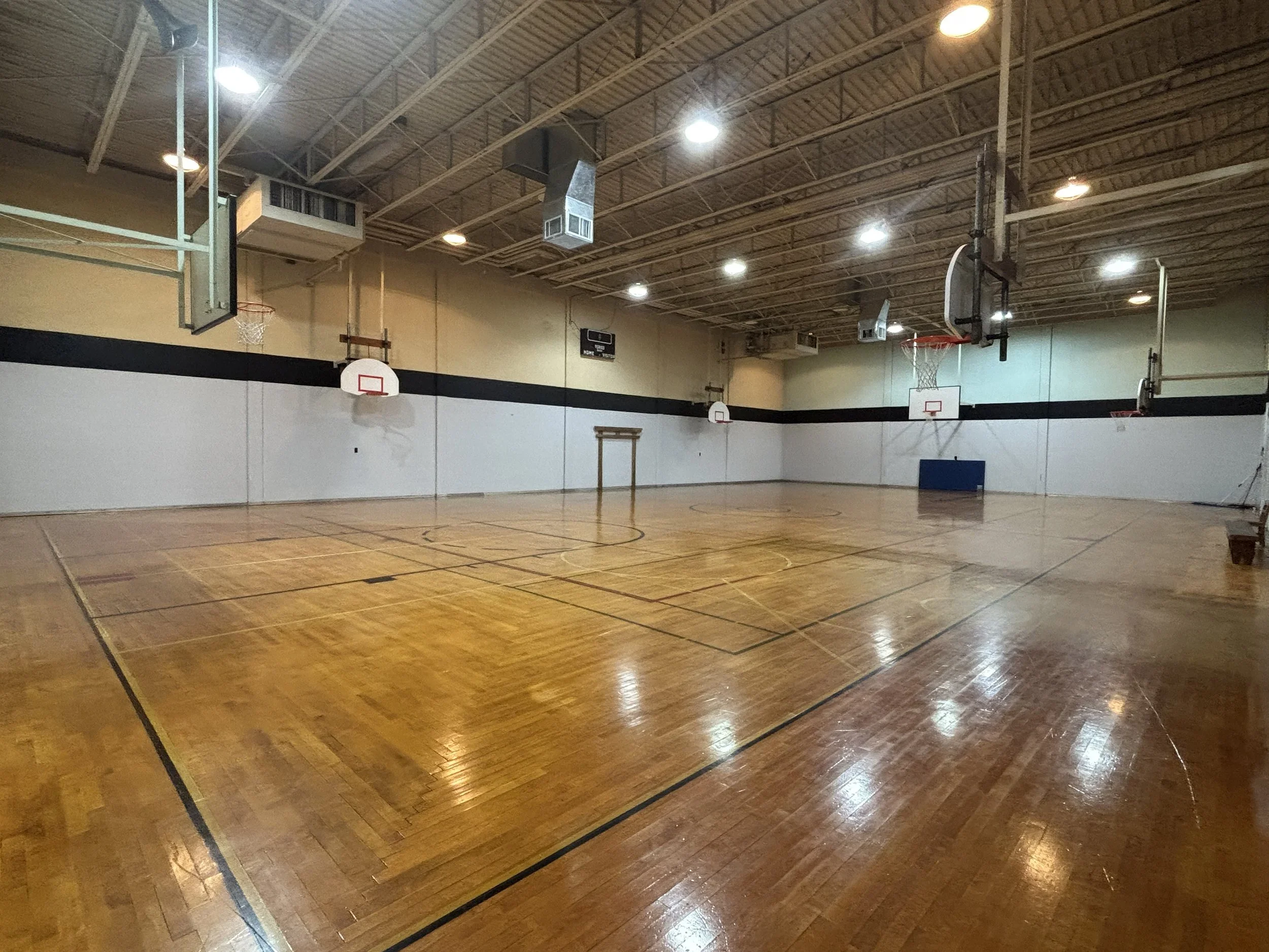 Indoor basketball court with hardwood flooring, basketball hoops, and ceiling lights.