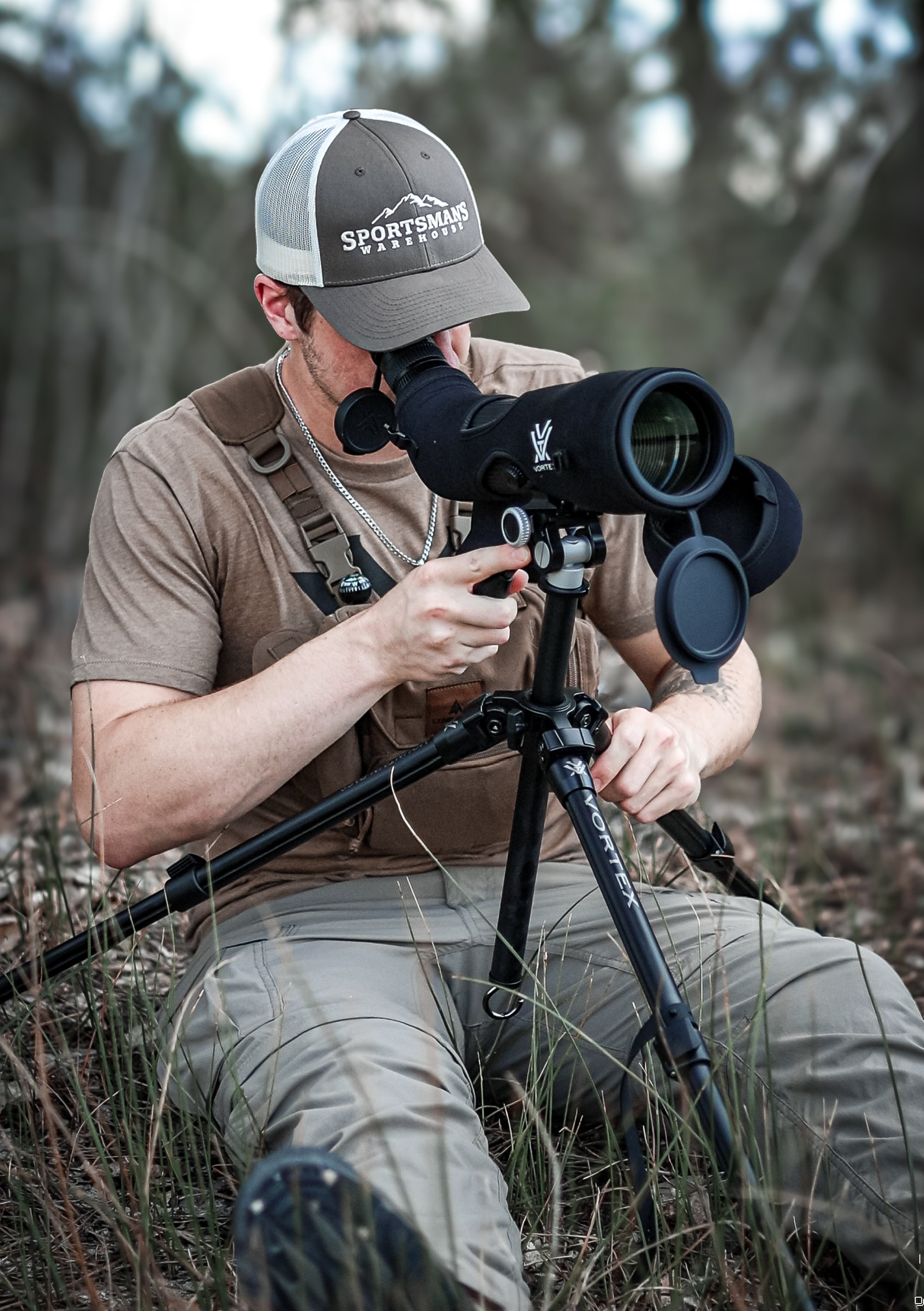 A man sitting outdoors at dusk, looking through a spotting scope mounted on a tripod, wearing a cap, beige shirt, and khaki pants.