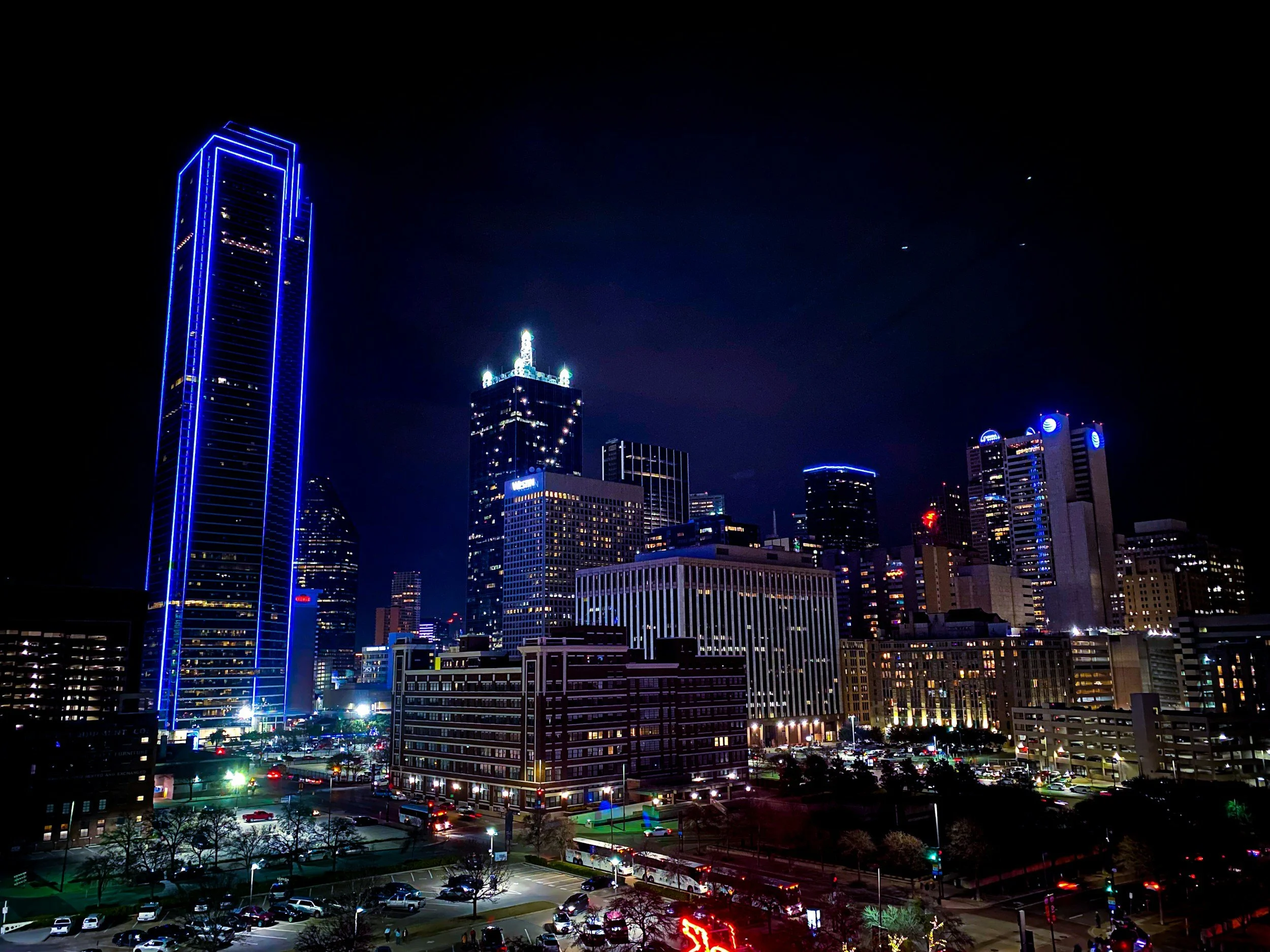Night city skyline with tall buildings outlined in blue neon lights and several star-like lights in the dark sky.