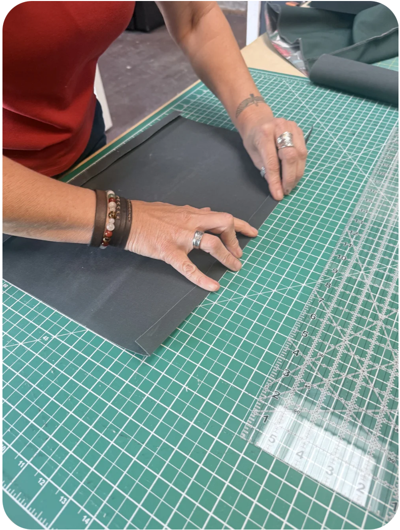 Person folding canvas material on a green cutting mat with a clear ruler and a work surface, while making a hand-made bag in a bag-making class.