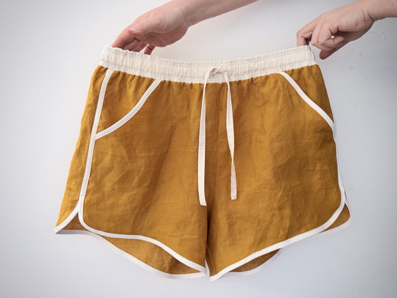 Person holding up a pair of handmade shorts with light coloured waistband and drawstrings and dark yellow material