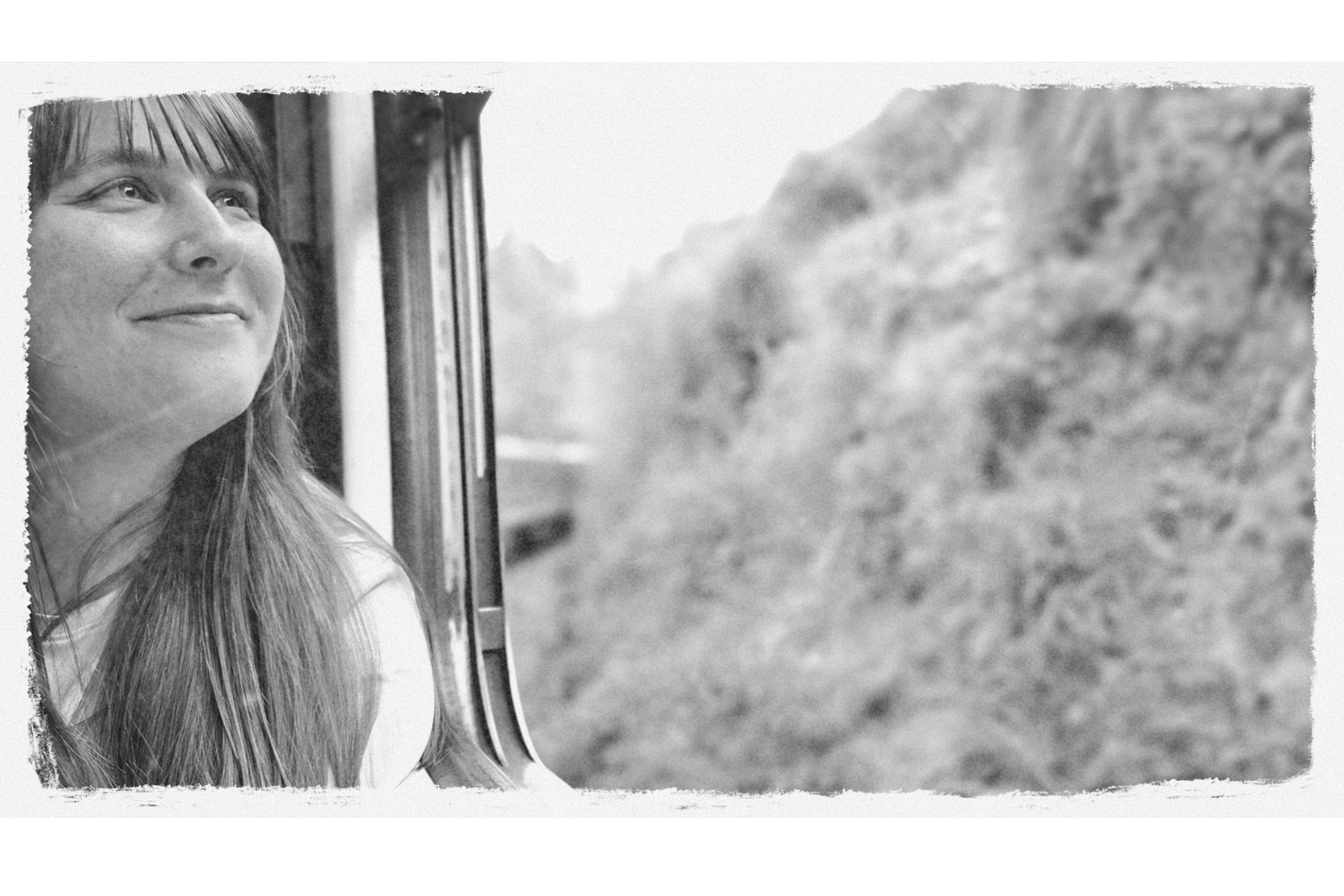 A woman with long hair looking out a window with mountain scenery in the background.