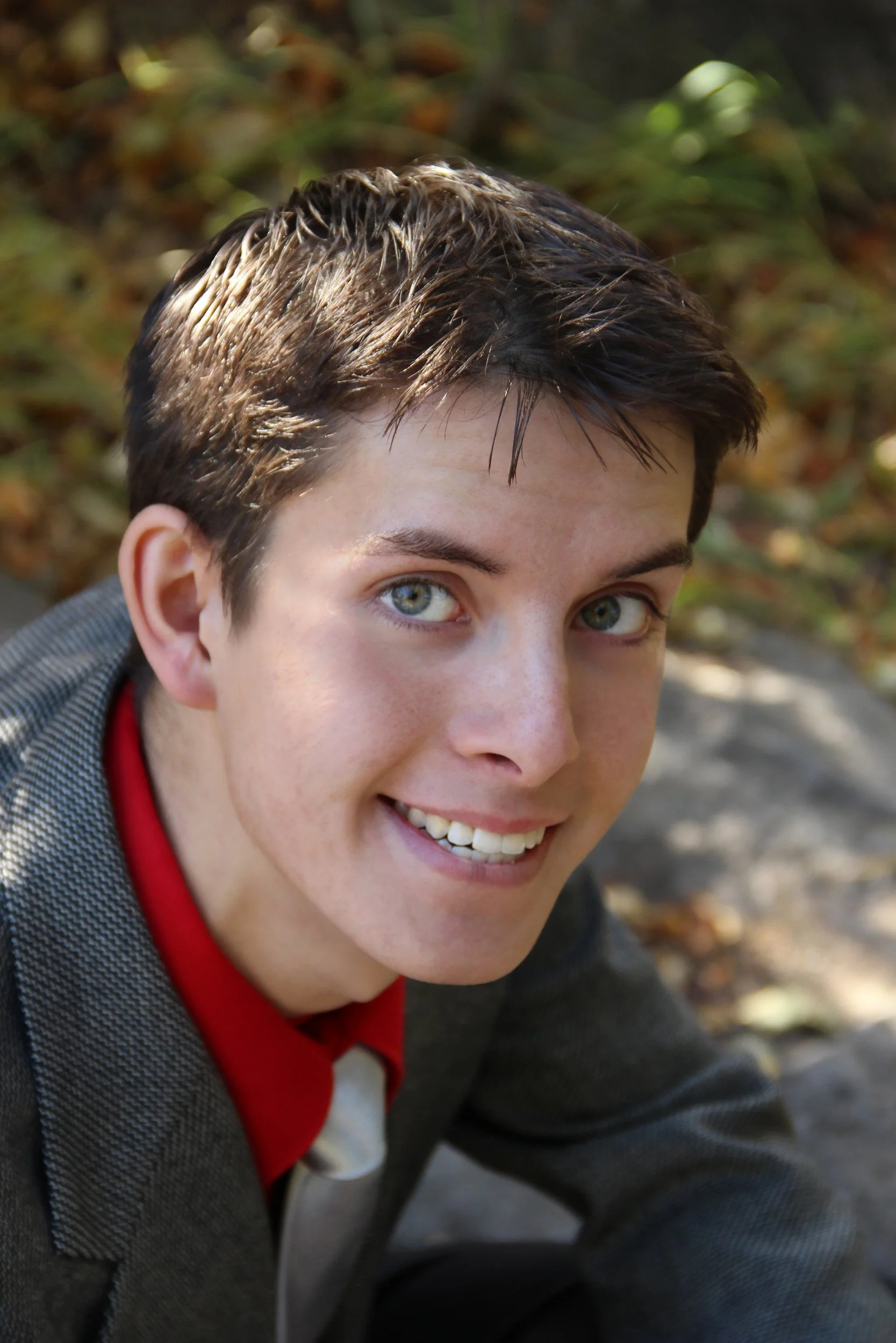 Senior portrait of Joseph Loveland smiling outdoors in the autumn, featuring his dark hair, incredible smile, and bright blue eyes