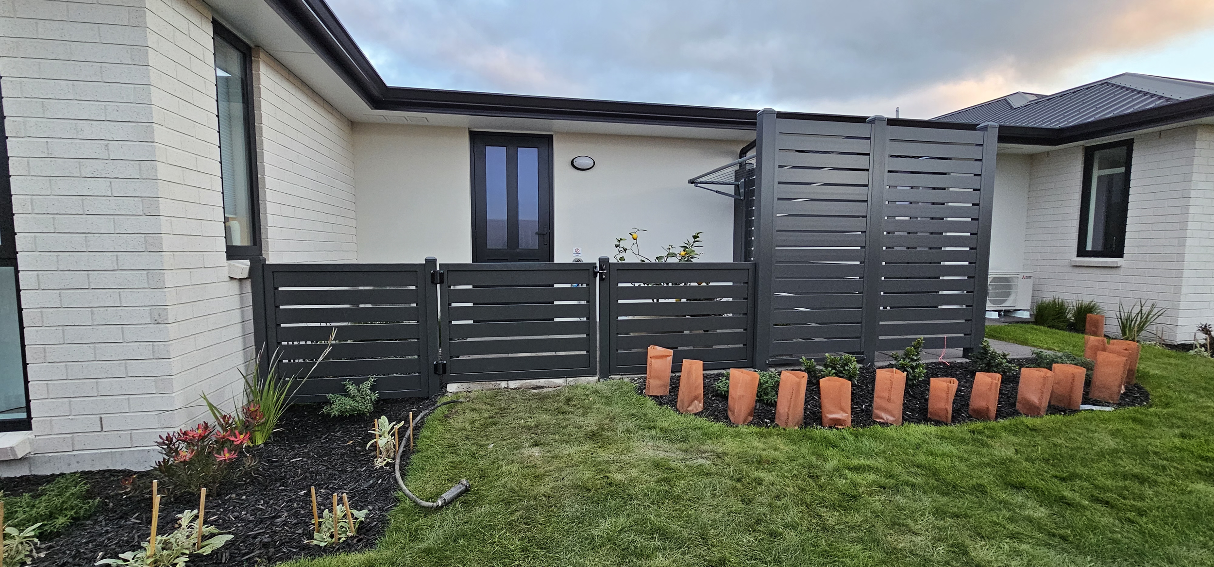 Black aluminium slat driveway gate at dusk