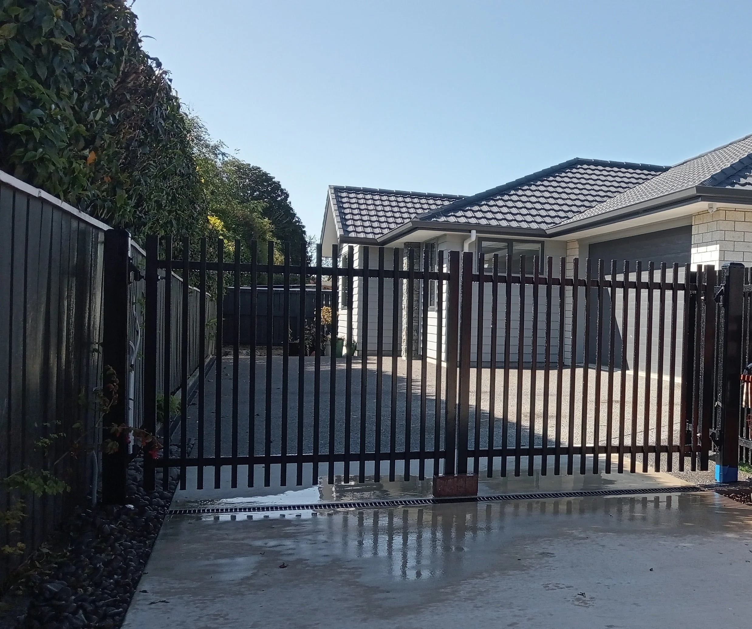Modern black slat fence and automated sliding gate at a Northland home