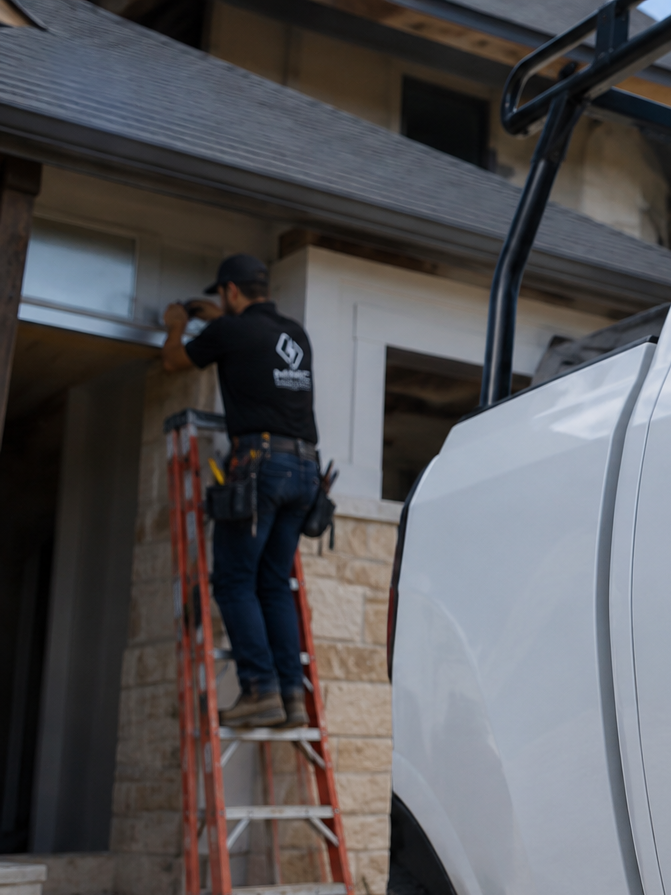 A construction worker standing on a ladder and installing or repairing something on the exterior of a house.