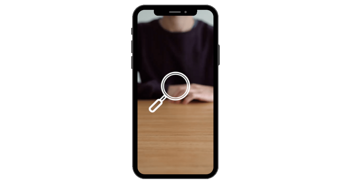 Smartphone screen showing a person sitting at a table with a magnifying glass icon over the image.