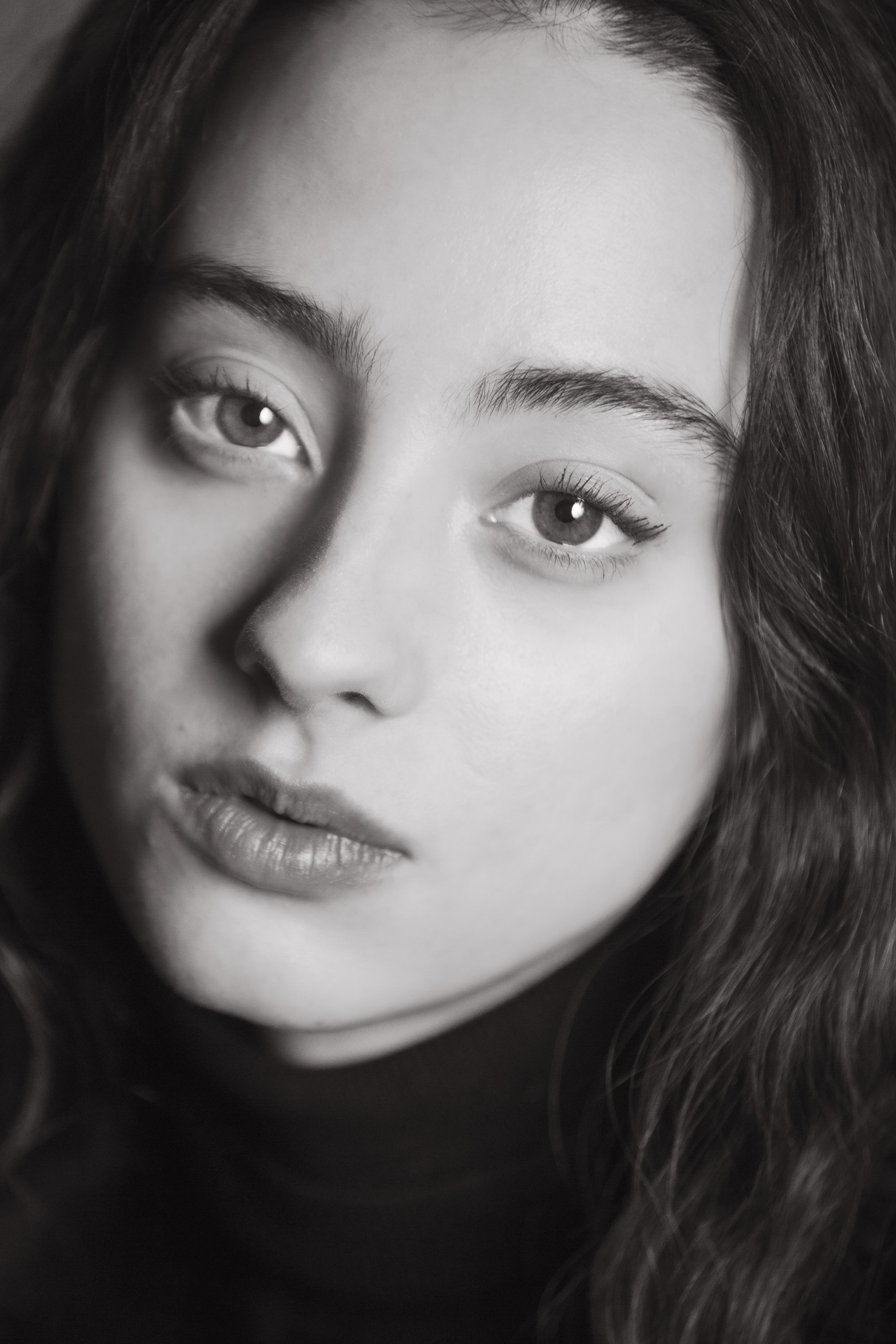 Close-up black and white portrait of a woman's face, focusing on her eyes, nose, and mouth. Her hair is visible partially on the right side of the image.