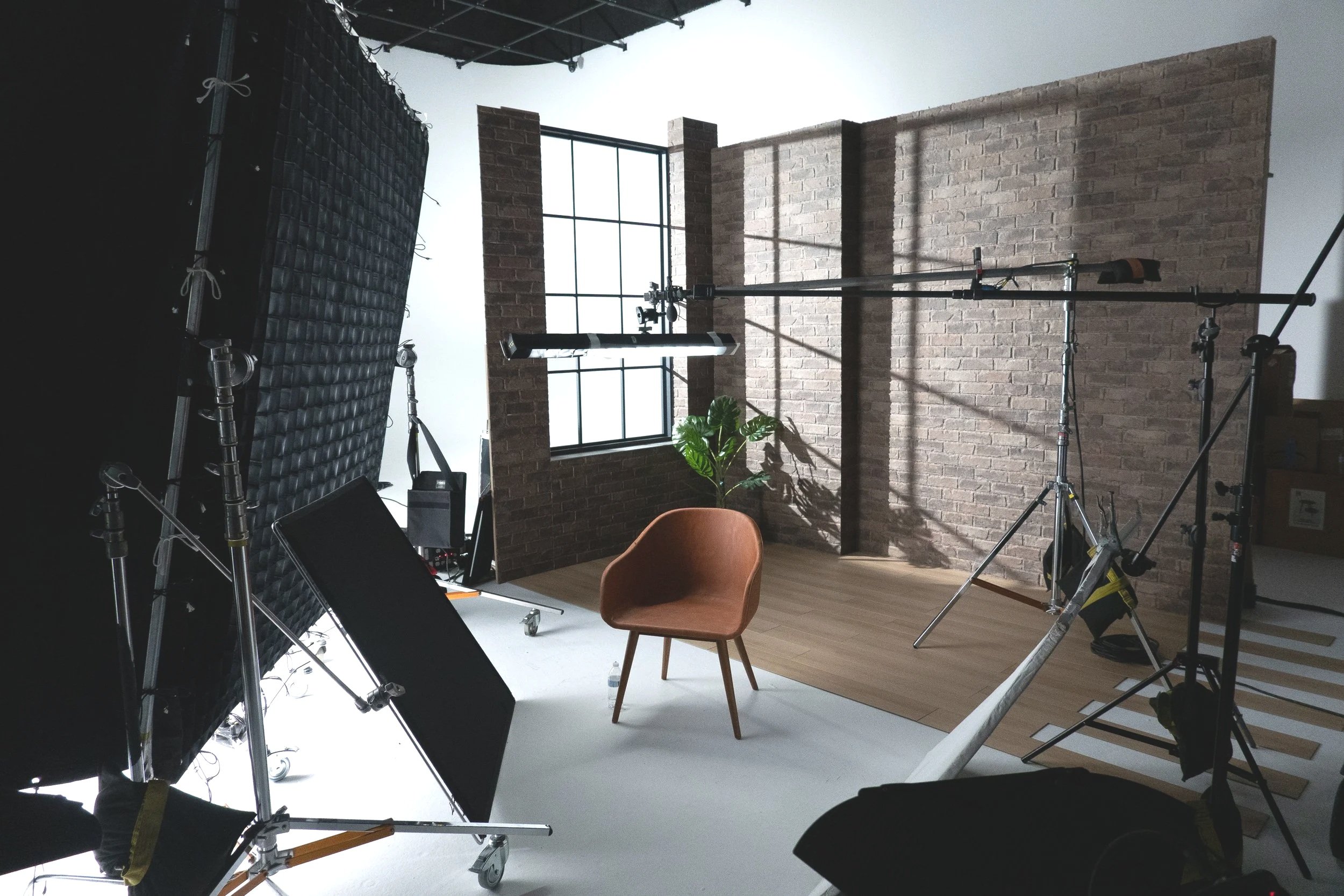 Photography studio with professional lighting, a brown chair, a potted plant, brick walls, and a large window