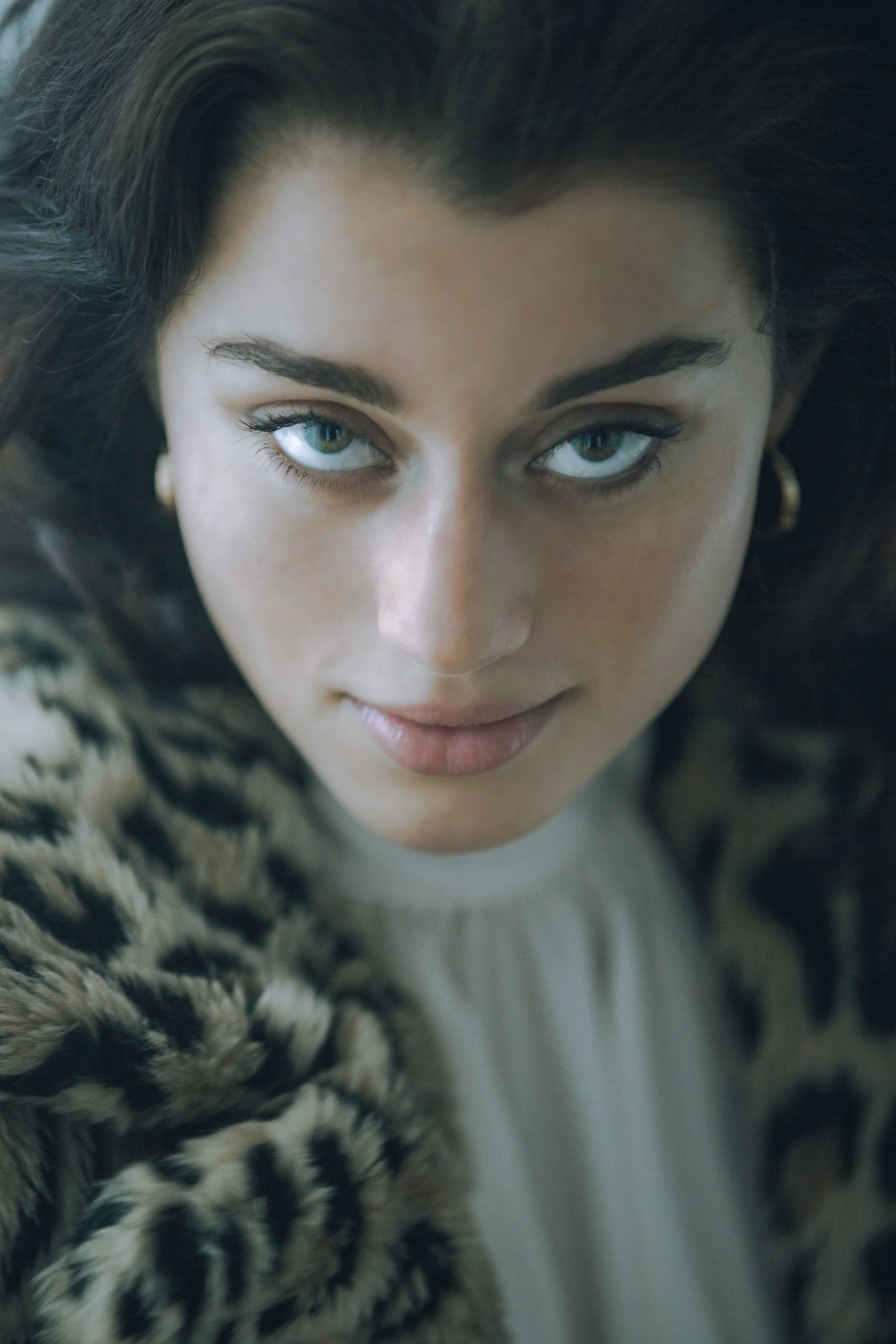 Close-up of a woman with striking blue eyes, dark hair, and wearing a leopard print garment.