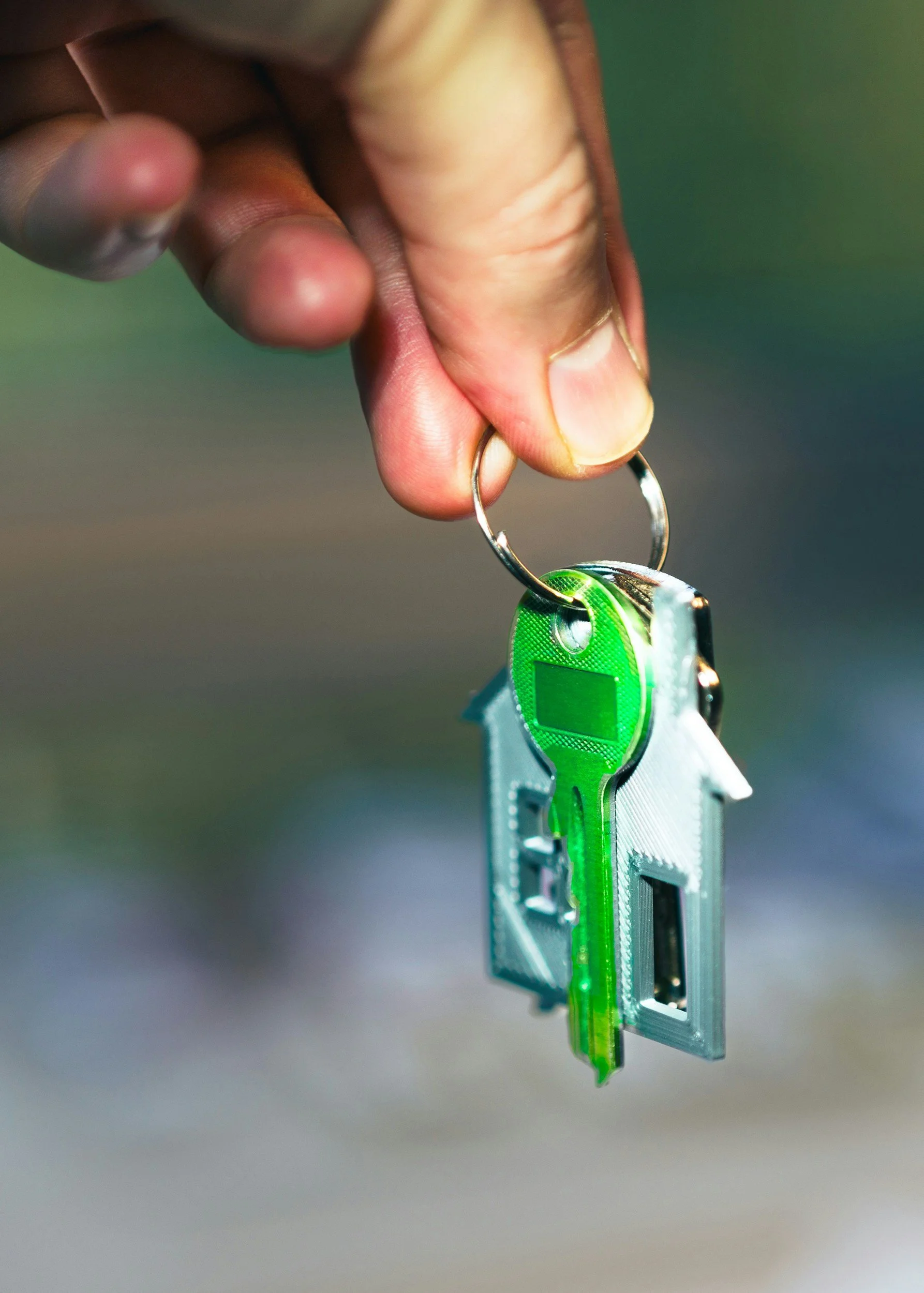 Close-up image of a hand holding a keychain with multiple keys, including a bright green key, against a blurred background.