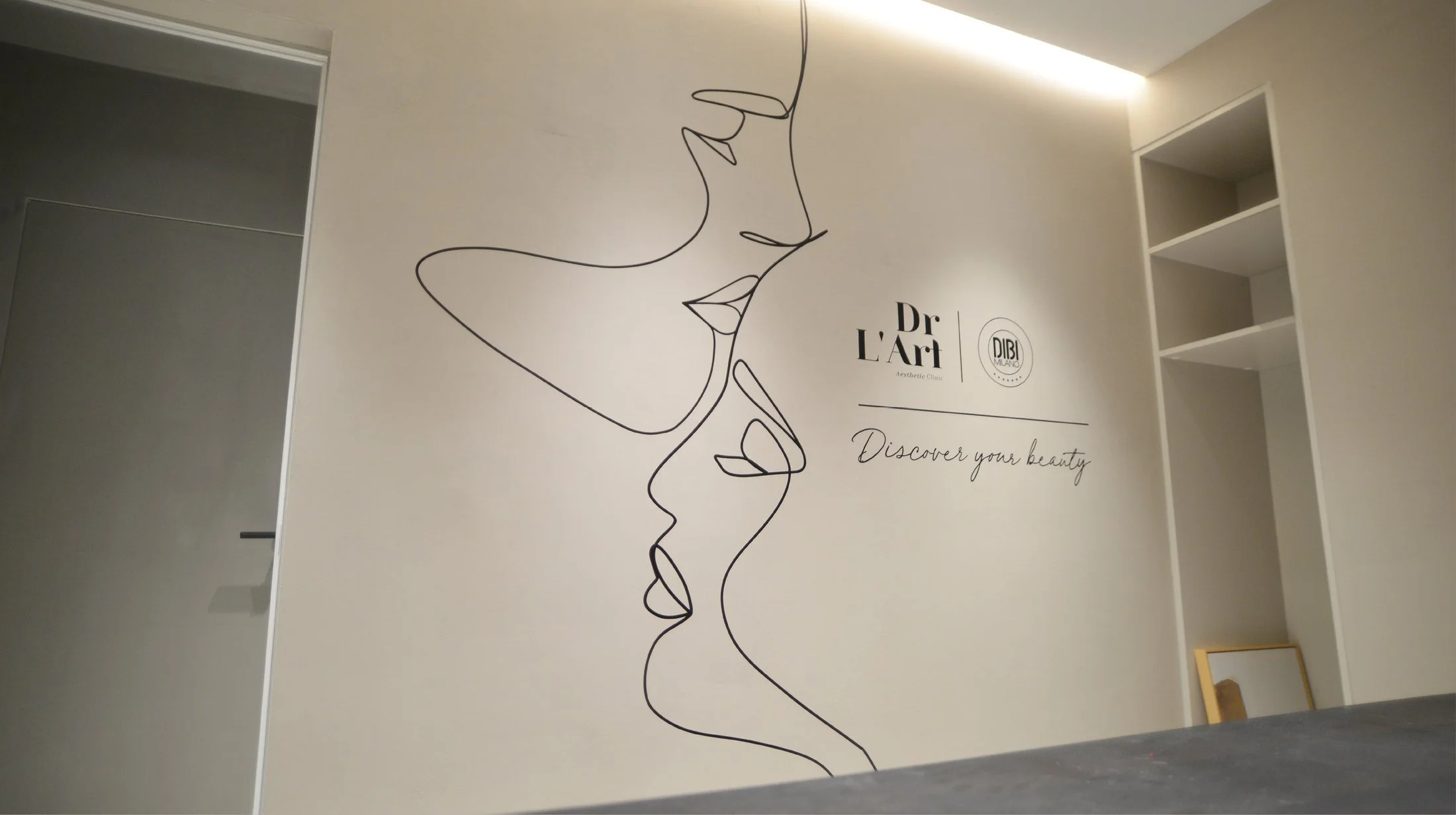 Minimalist line art of two faces in profile, intertwined on a white wall. Text reads "Dr L'Art Aesthetic Clinic" and "Discover your beauty."