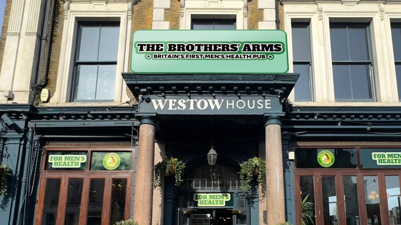 Exterior of Westow House, a pub with signs indicating it is for men's health, located in a building with tall windows and decorative architecture, with hanging greenery at the entrance.