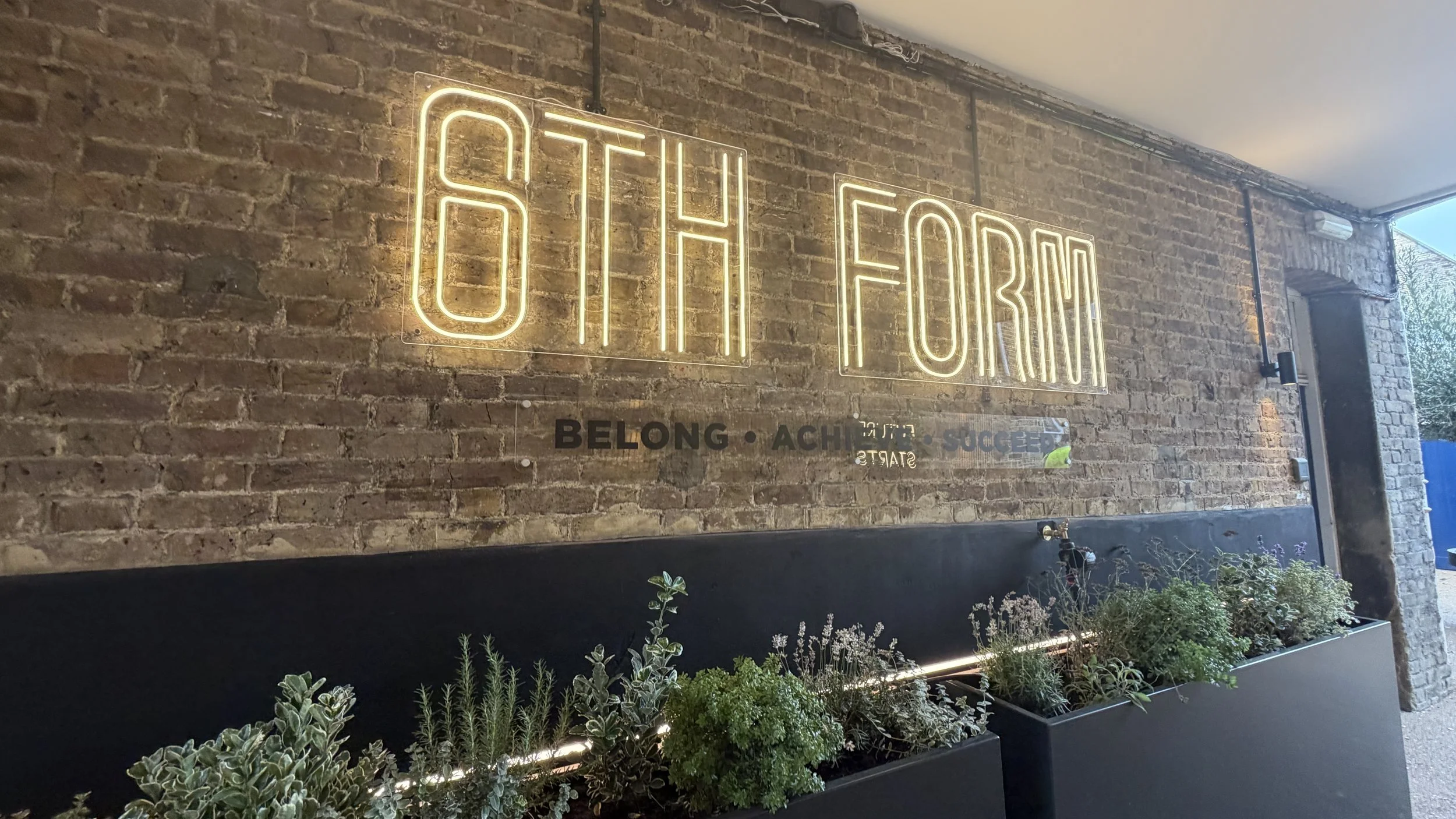 Large illuminated sixth form sign with Belong Achieve Succeed lettering on exposed brick wall.JPG
