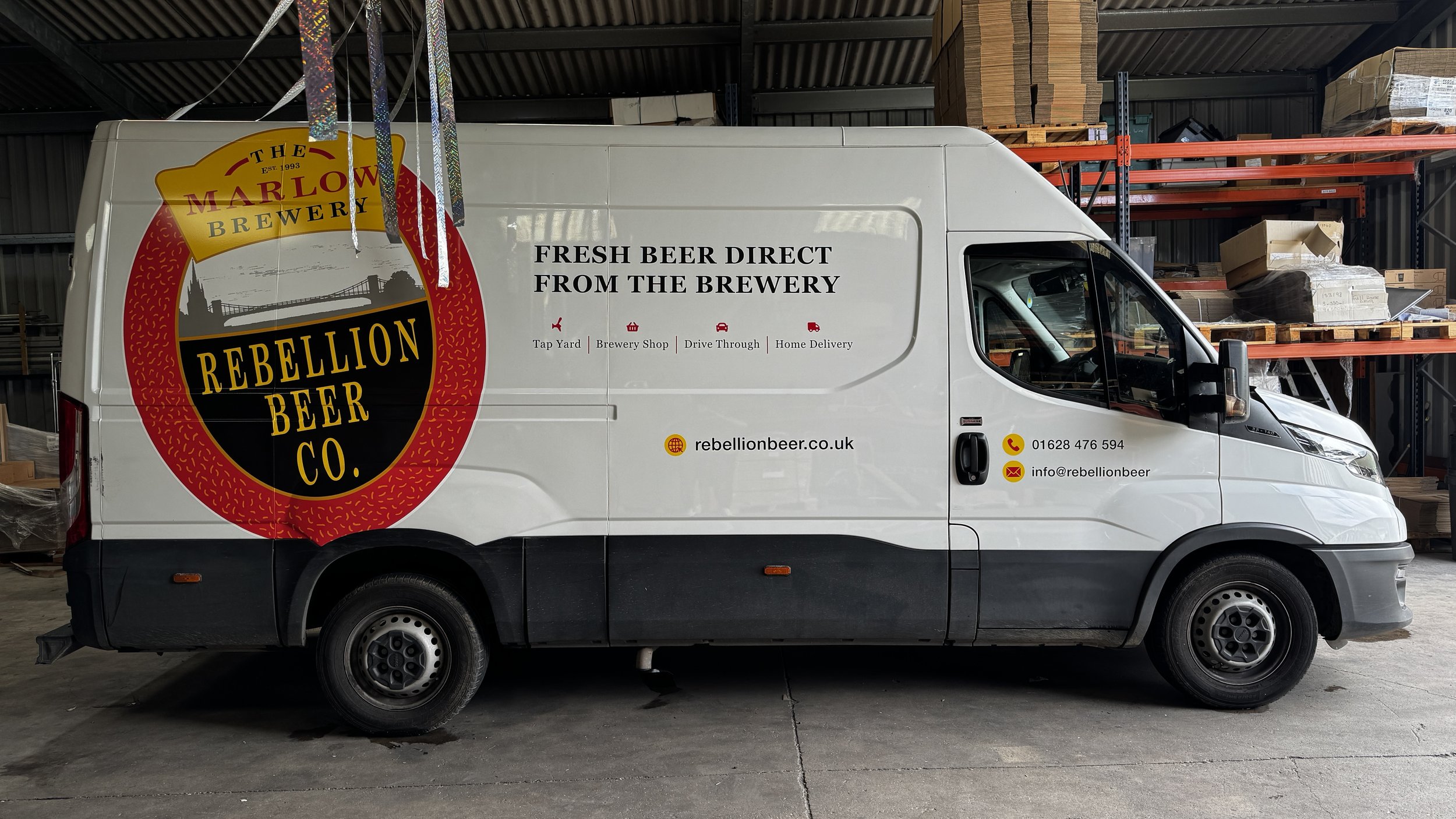 White delivery van with Rebellion Beer Co. logo and contact information, parked inside a warehouse.