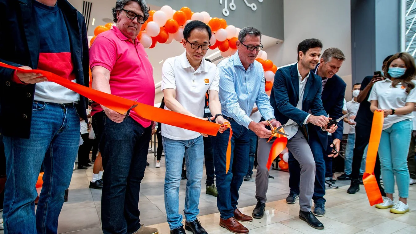Group of people participating in a ribbon-cutting ceremony indoors, with balloons and decorations in the background.