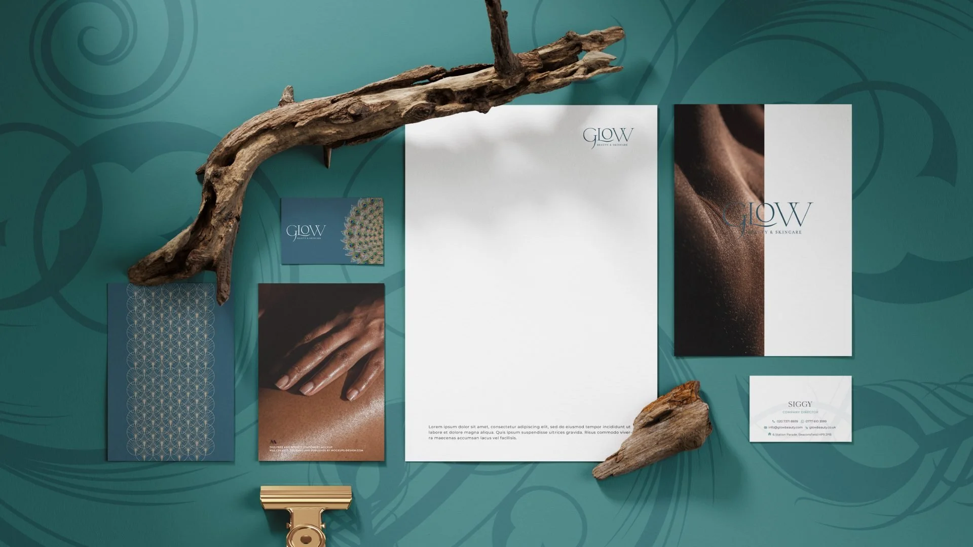 Flat lay of branding materials, including brochures, business card, and paper, on a teal background with abstract swirl patterns, accented by driftwood and a gold paper clip.