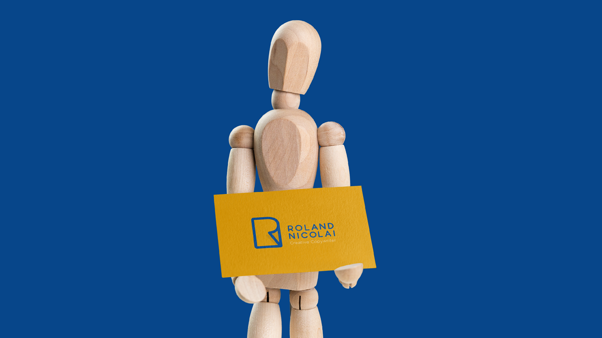 A-wooden-mannequin-holding-a-business-card-with-Roland-Nicolai-branding-on-1.png