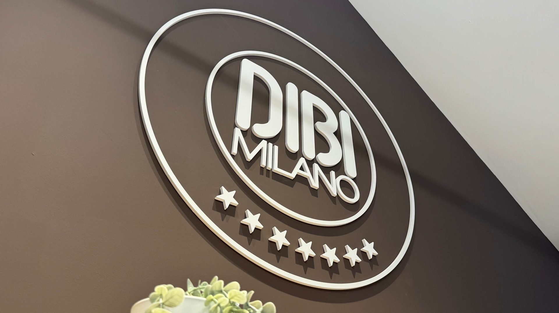 Close-up of a decorative wall sign that reads 'DUBAI MILANO' with five stars beneath it, mounted on a brown wall.