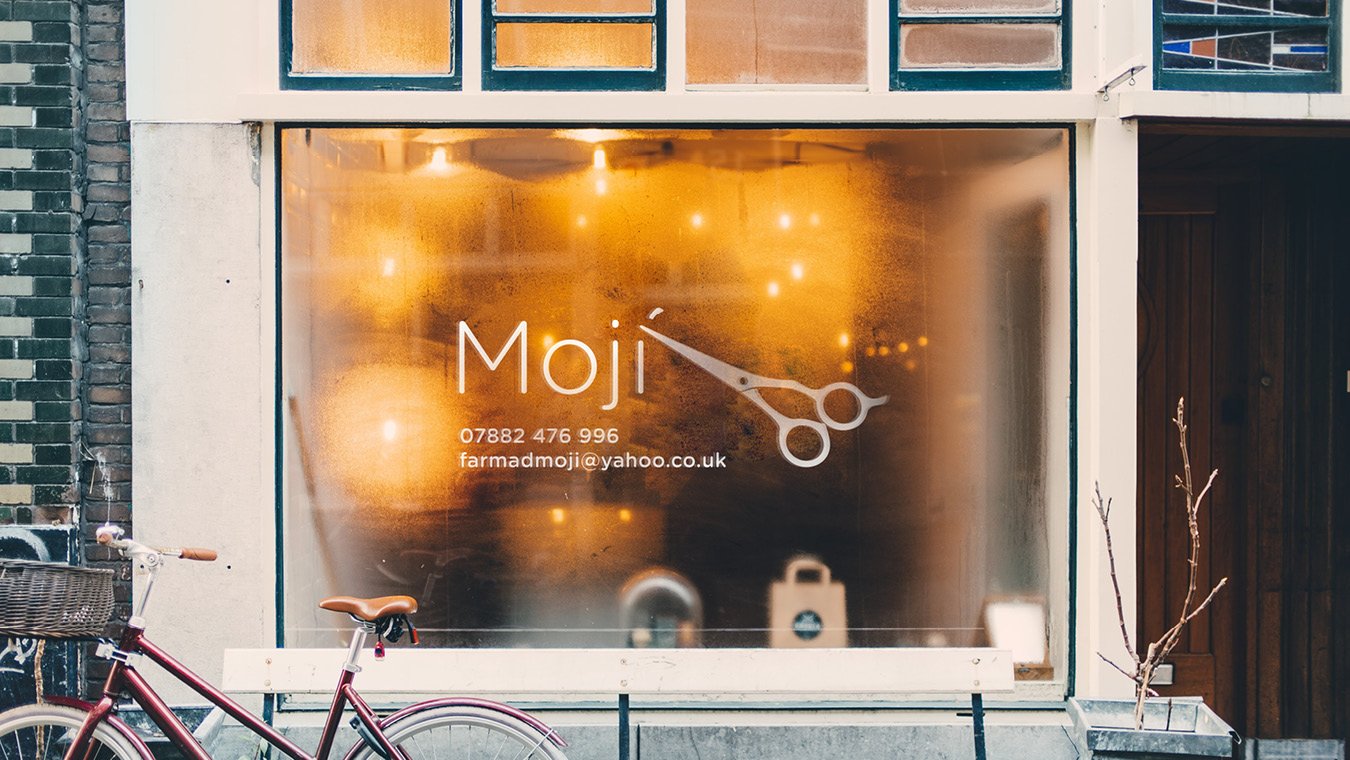  storefront window with the word 'Moji' and a pair of scissors graphic, contact details, and a bicycle parked outside