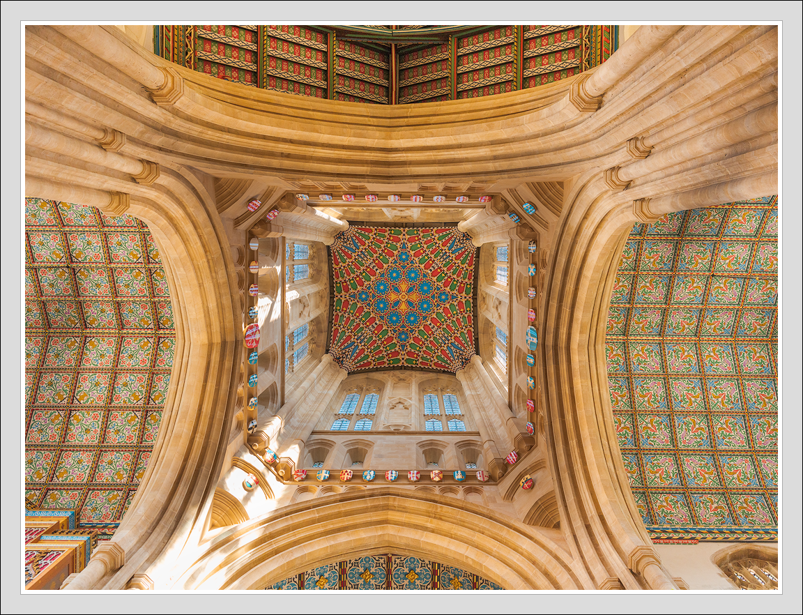 Looking up inside a cathedral showing ornate stone arches and a colorful, patterned ceiling with intricate tilework.