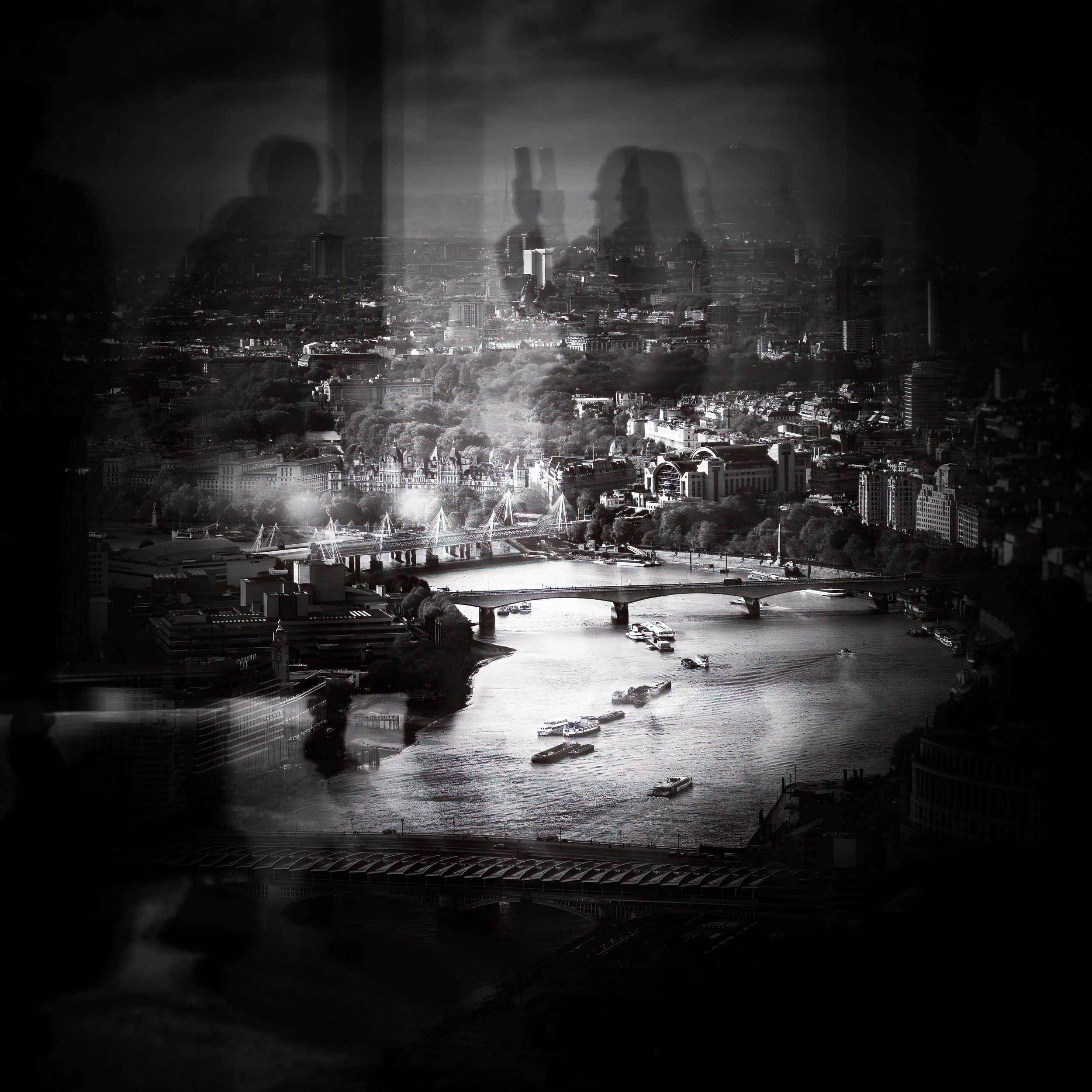 A cityscape at night with buildings, a river, and bridges, viewed through a window with reflections of three people.