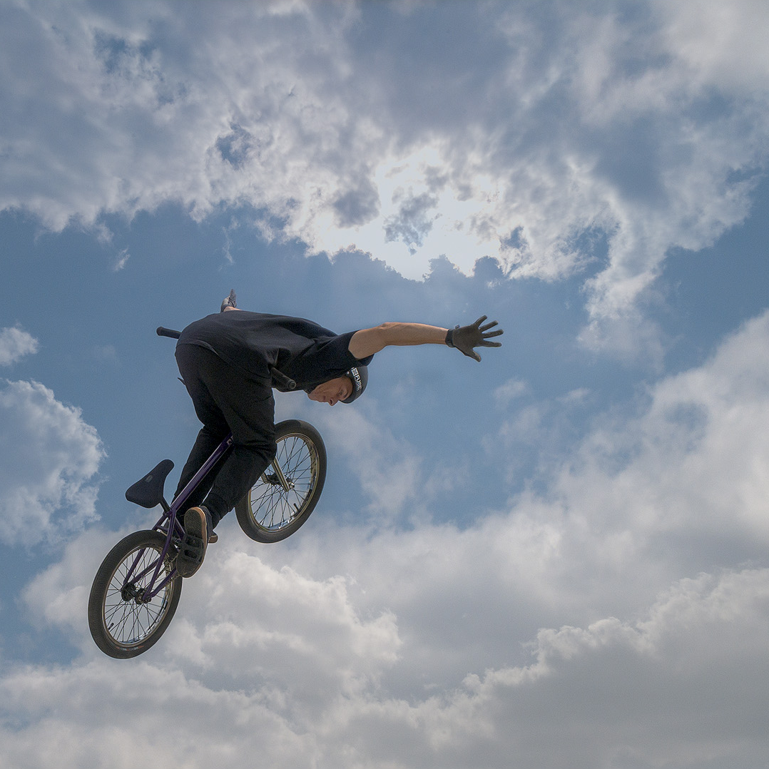 A person performing a stunt on a BMX bike in the air against a cloudy sky.