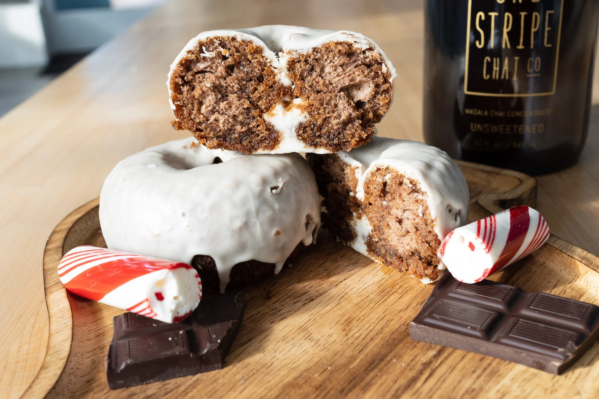 Ice cream sandwich with chocolate cookies and vanilla ice cream, placed on a wooden tray, with assorted candies and a chocolate bar in the background.