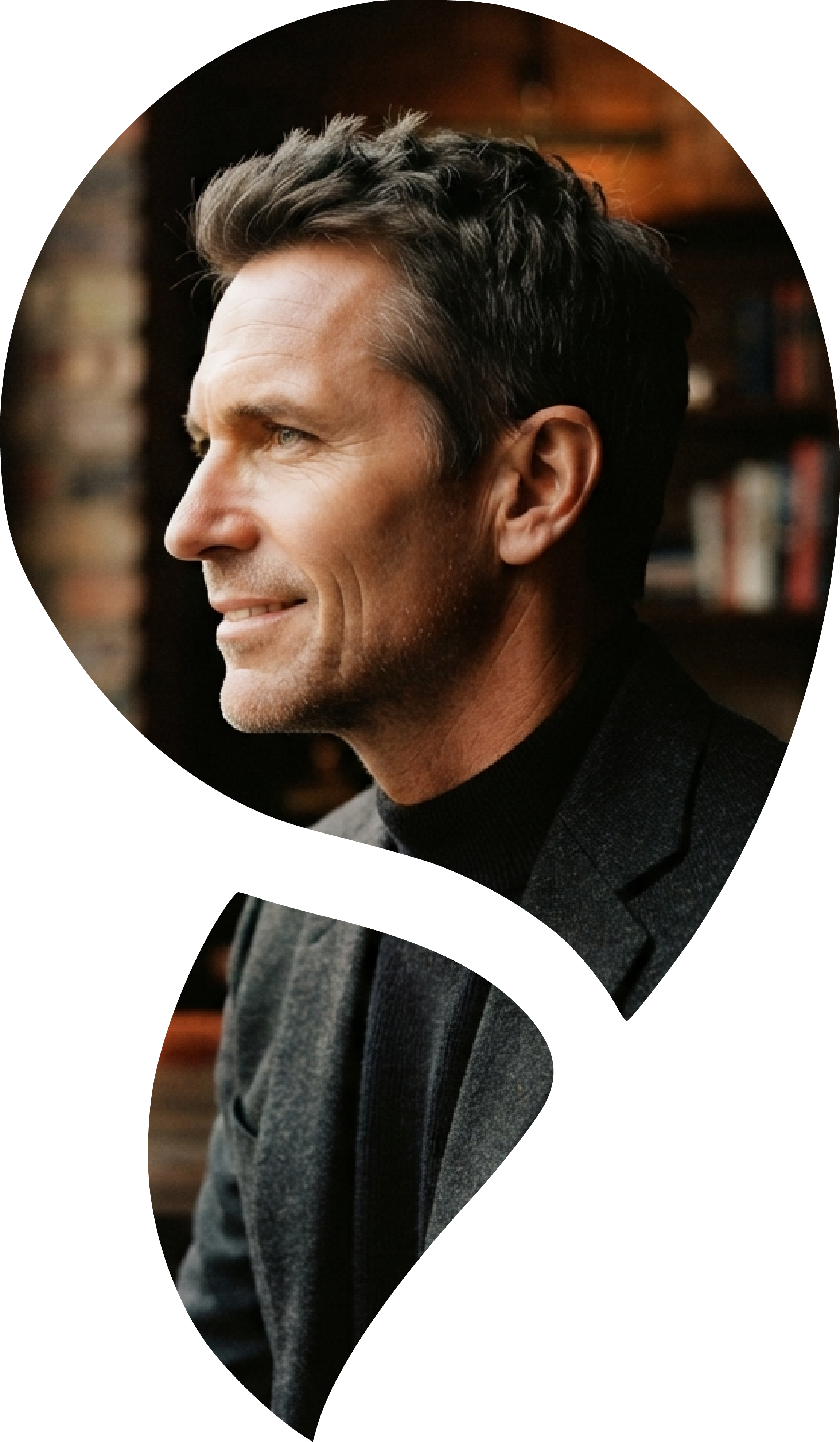 Profile of a middle-aged man with dark hair, wearing a black turtleneck and a gray blazer, in an indoor setting with blurred background.